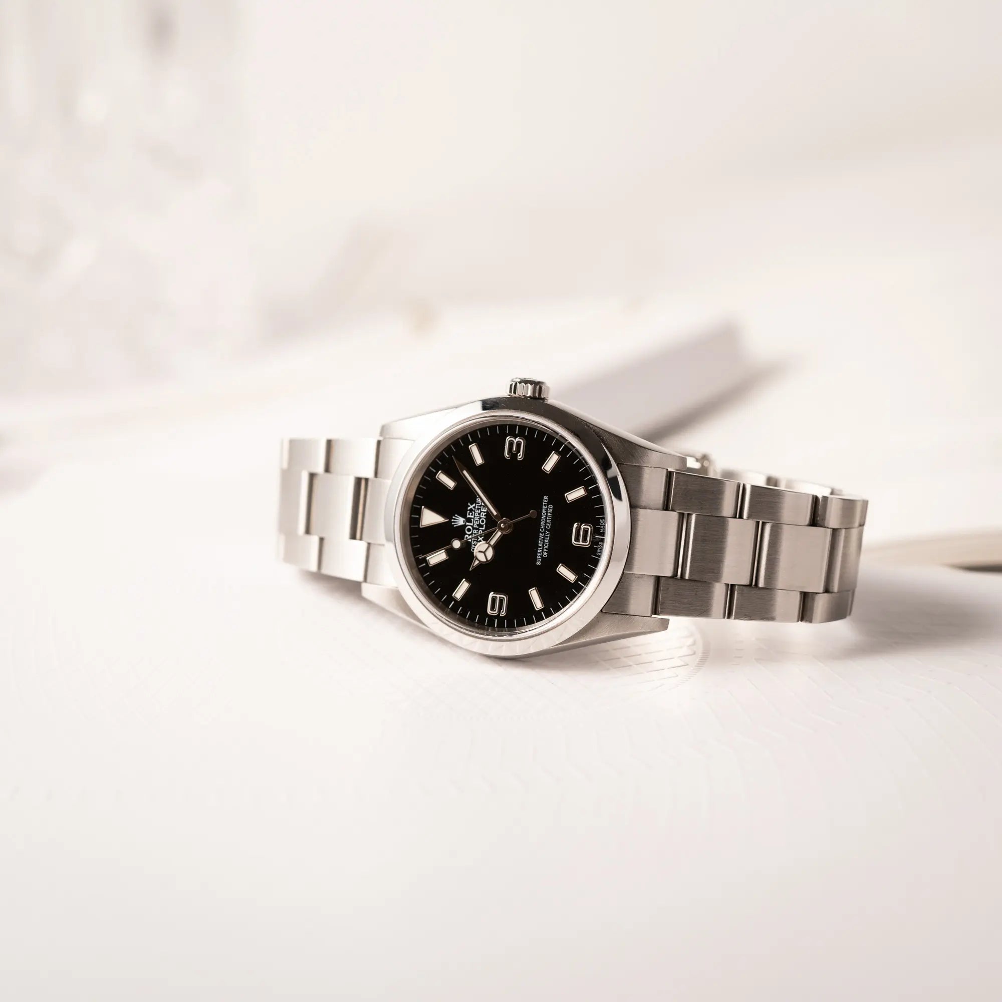 Produktfotografie der seitlich auf dem Uhrengehäuse liegenden Rolex Explorer 36 der Referenz 114270 mit dem klassischen schwarzen 3-6-9-Explorer-Zifferblatt am Oyster-Stahlband