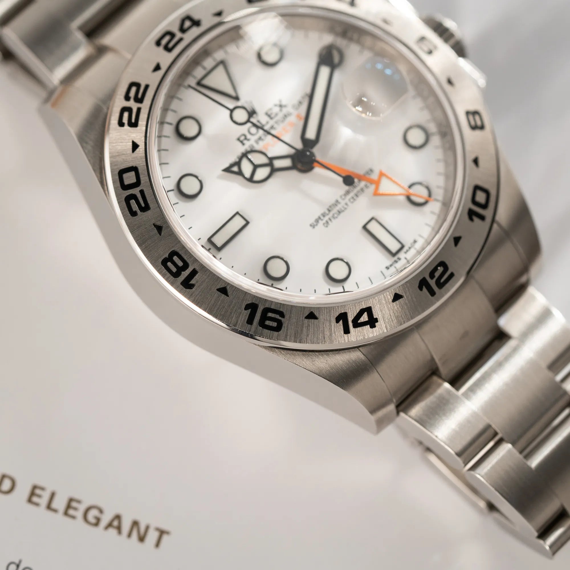 Produktfotografie der Rolex Explorer II 216570 aus 2021 mit dem weißen Polar Zifferblatt mit dem typischen orangen GMT-Zeiger in einem sehr guten Zustand mit Fokus auf der Lünette