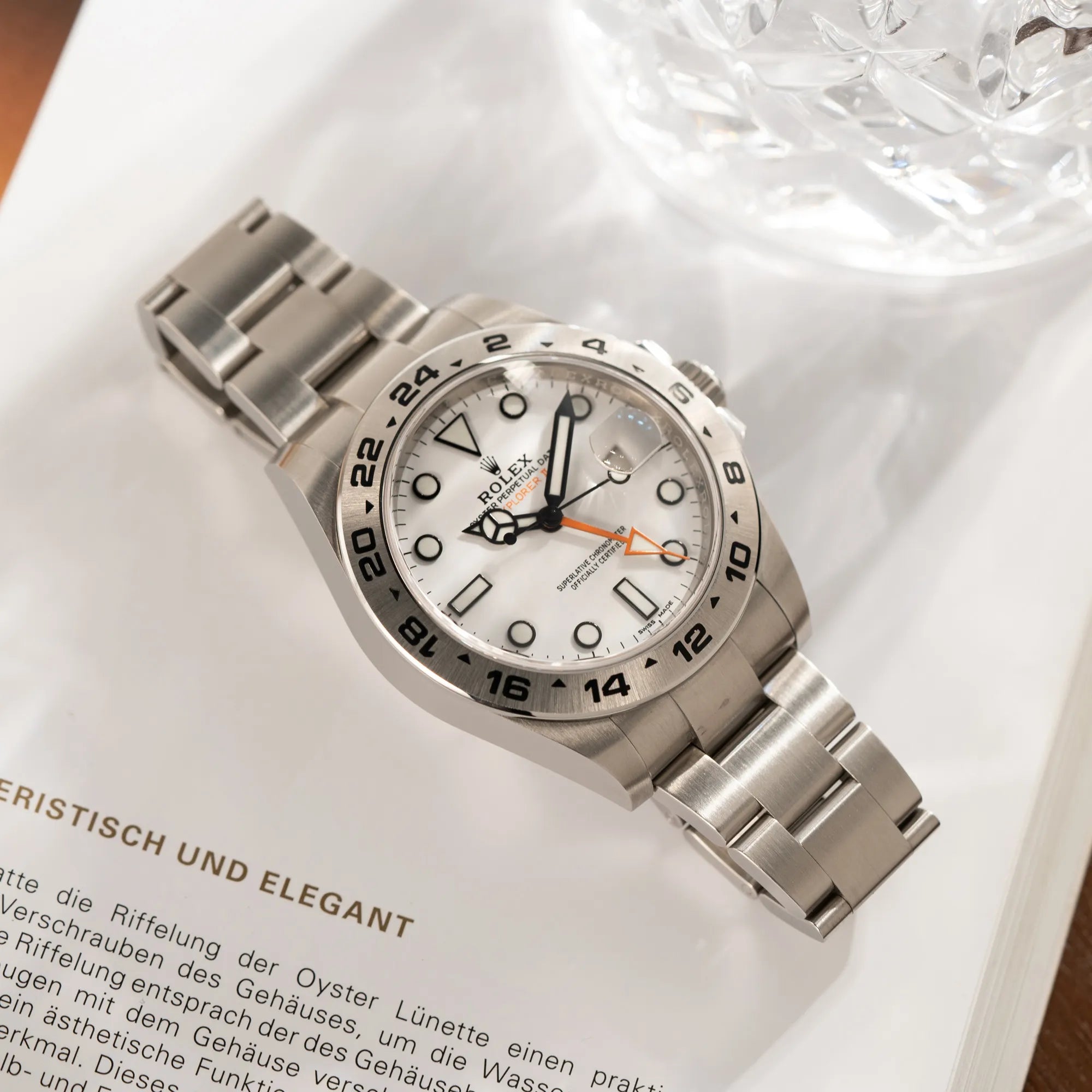 Produktfotografie der Rolex Explorer II 216570 aus 2021 mit dem weißen Polar Zifferblatt mit dem typischen orangen GMT-Zeiger in einem sehr guten Zustand, während diese flach auf dem Uhrenband liegt