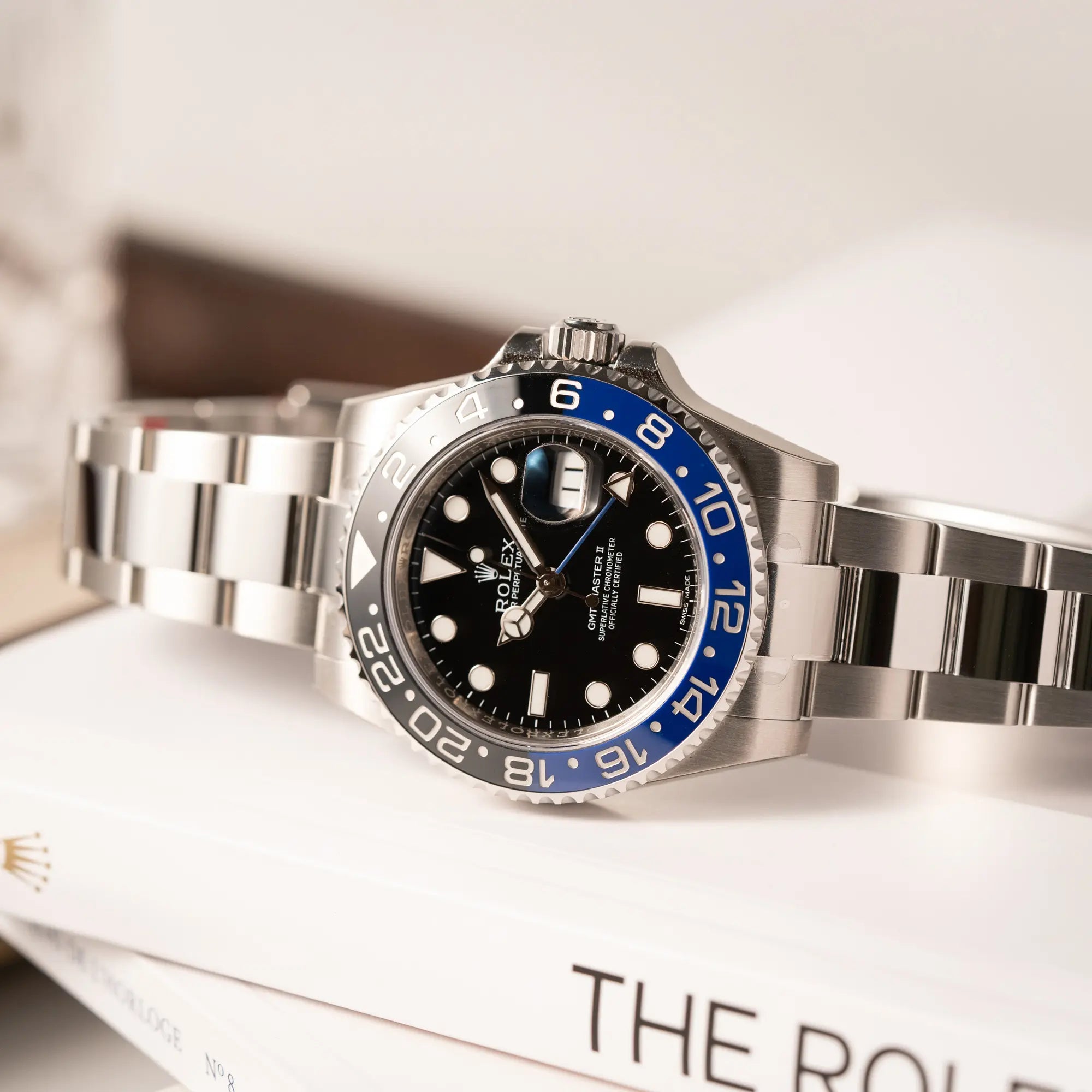 Produktfotografie der seitlich auf dem Uhrengehäuse liegenden Rolex GMT-Master II der Referenz 116710BLNR mit dem Nickname "Batman" mit der schwarz blauen Keramik-Lünette am Oyster-Stahlband im verklebten Neuzustand