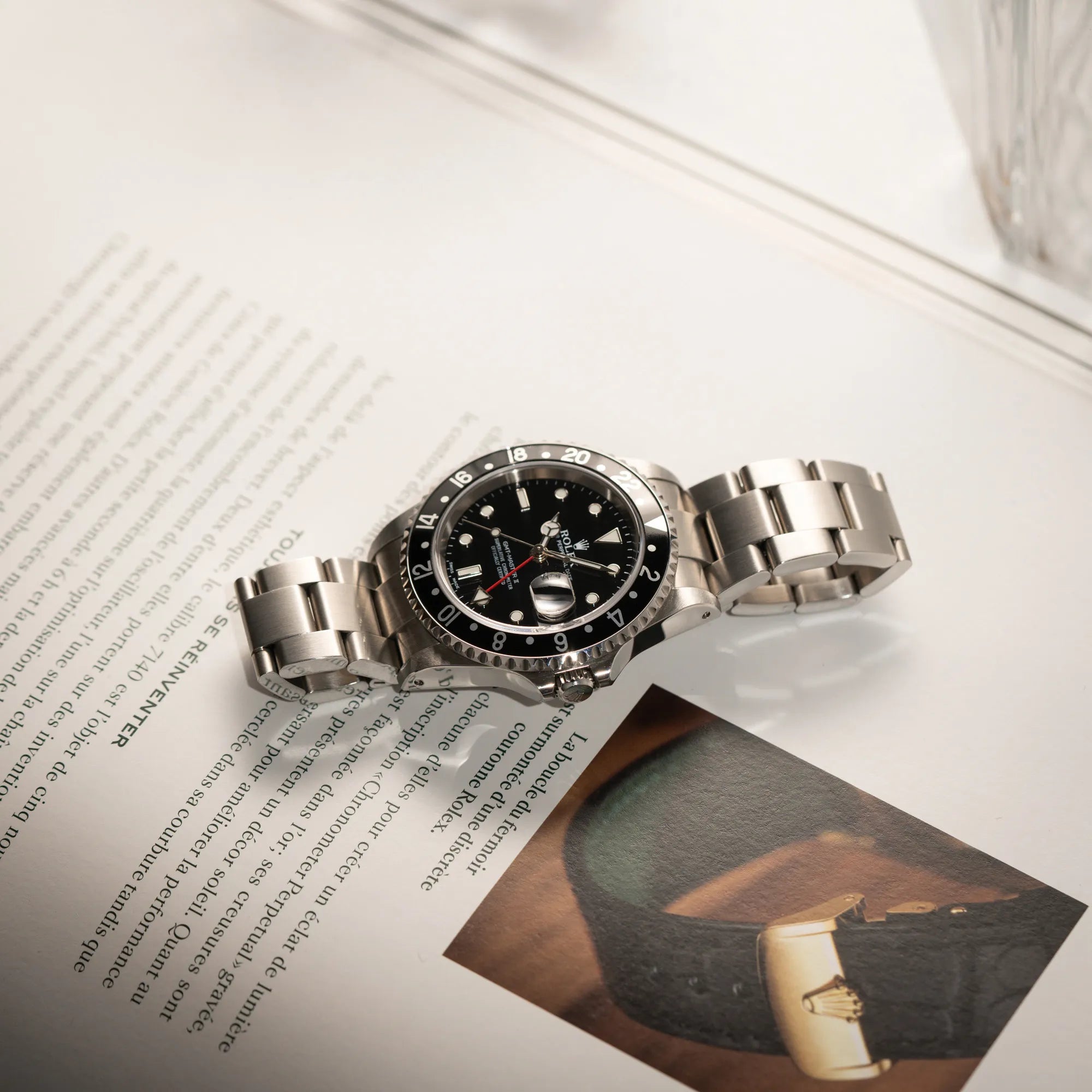 Produktfotografie der Rolex GMT-Master II 16710  aus 2001 mit schwarzem Aluminium-Lünetten-Inlay in einem neuwertigen Zustand während die Uhr auf einem Uhrenbuch über Rolex liegt