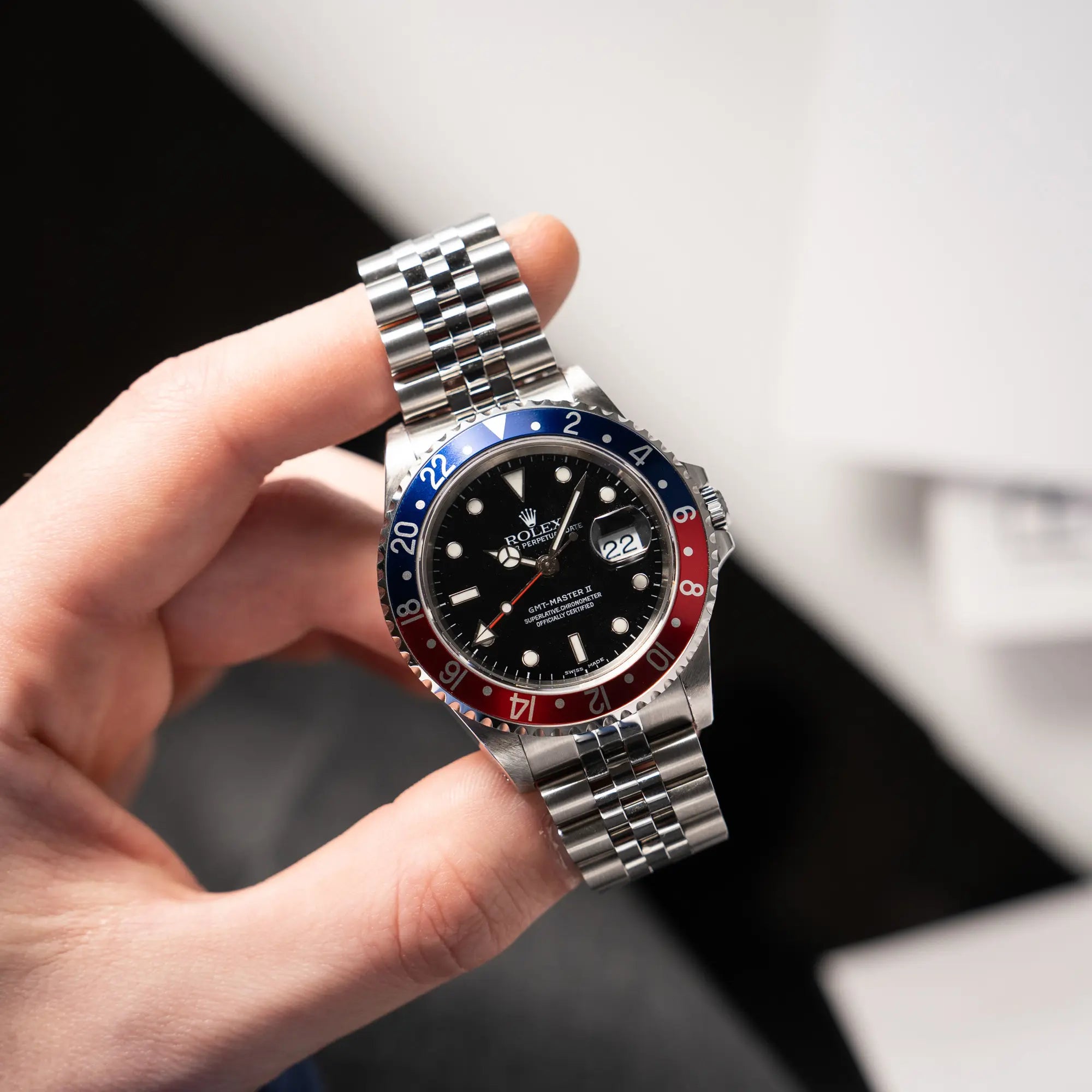 Mann hält die Rolex GMT-Master II 16710 mit der blau-roten Pepsi-Lünette am Jubilee-Armband zwischen seinen Fingern und präsentiert die Uhr in die Kamera