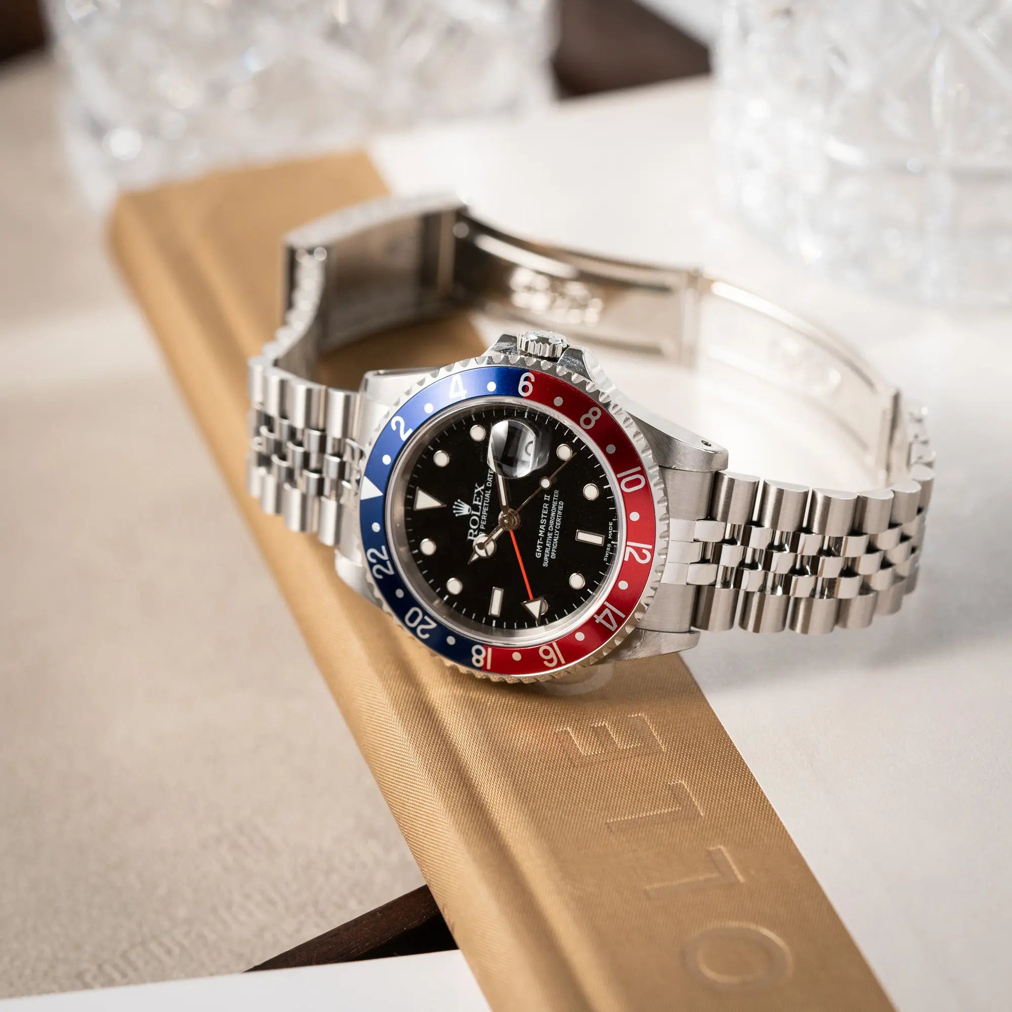 Produktfoto der Rolex GMT-Master II 16710 mit der blau-roten Pepsi-Lünette am Jubilee-Armband  während die Uhr mit geöffneter Schliesse auf einem Buch liegt