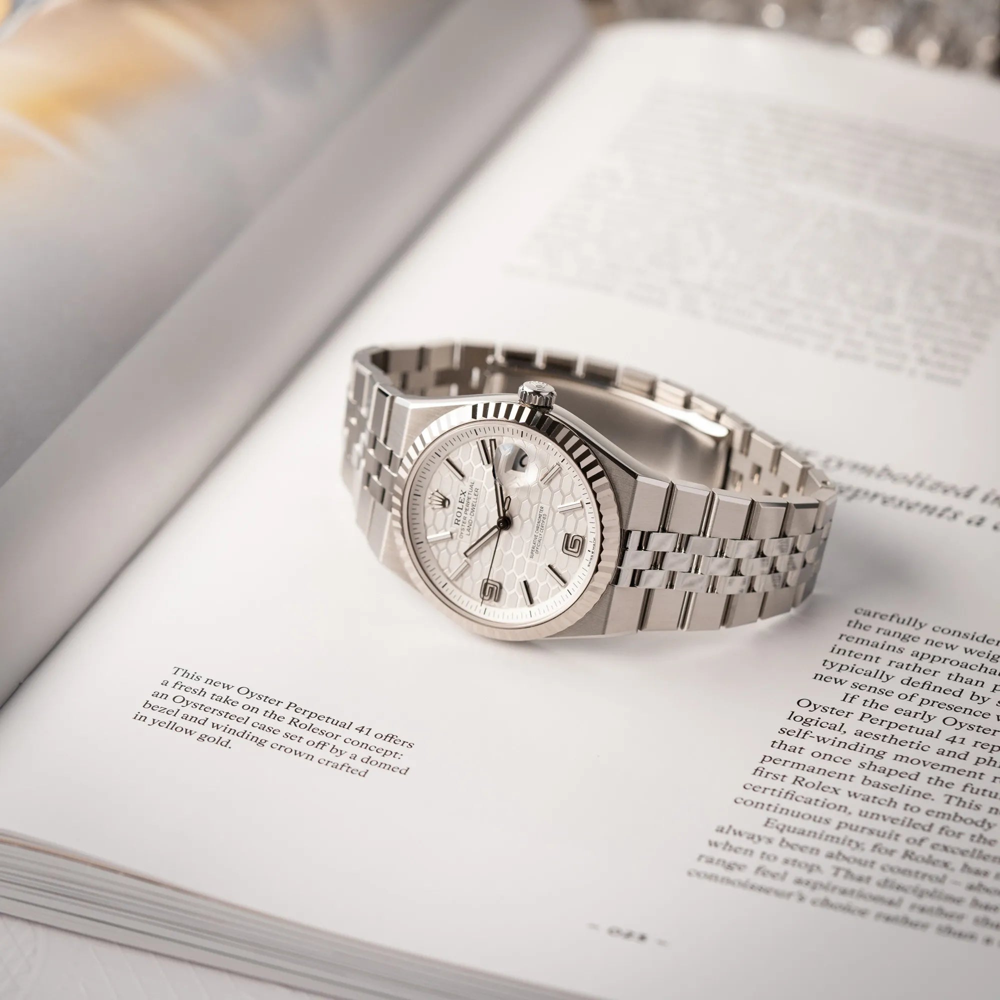 Rolex Land-Dweller 40 der Referenz 127334 im neuwertigen Zustand mit dem weißen Zifferblatt in Waben-Struktur am neuen Flat-Jubilee-Armband liegt auf einem Buch über Rolex-Uhren