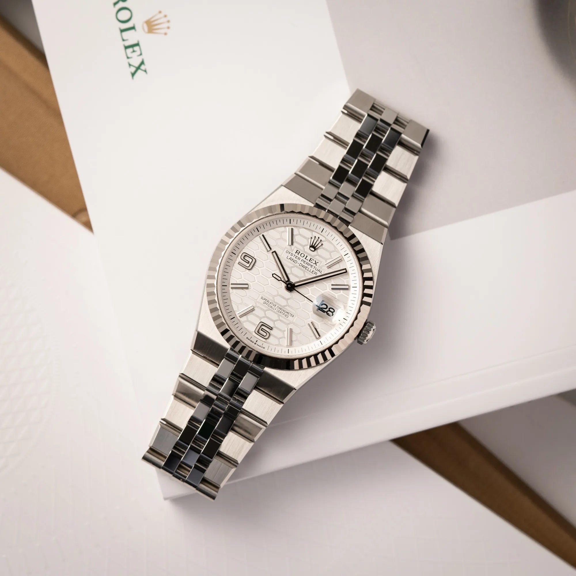 Rolex Land-Dweller 40 der Referenz 127334 im neuwertigen Zustand mit dem weißen Zifferblatt in Waben-Struktur am neuen Flat-Jubilee-Armband liegt flach auf dem Rolex-Magazin