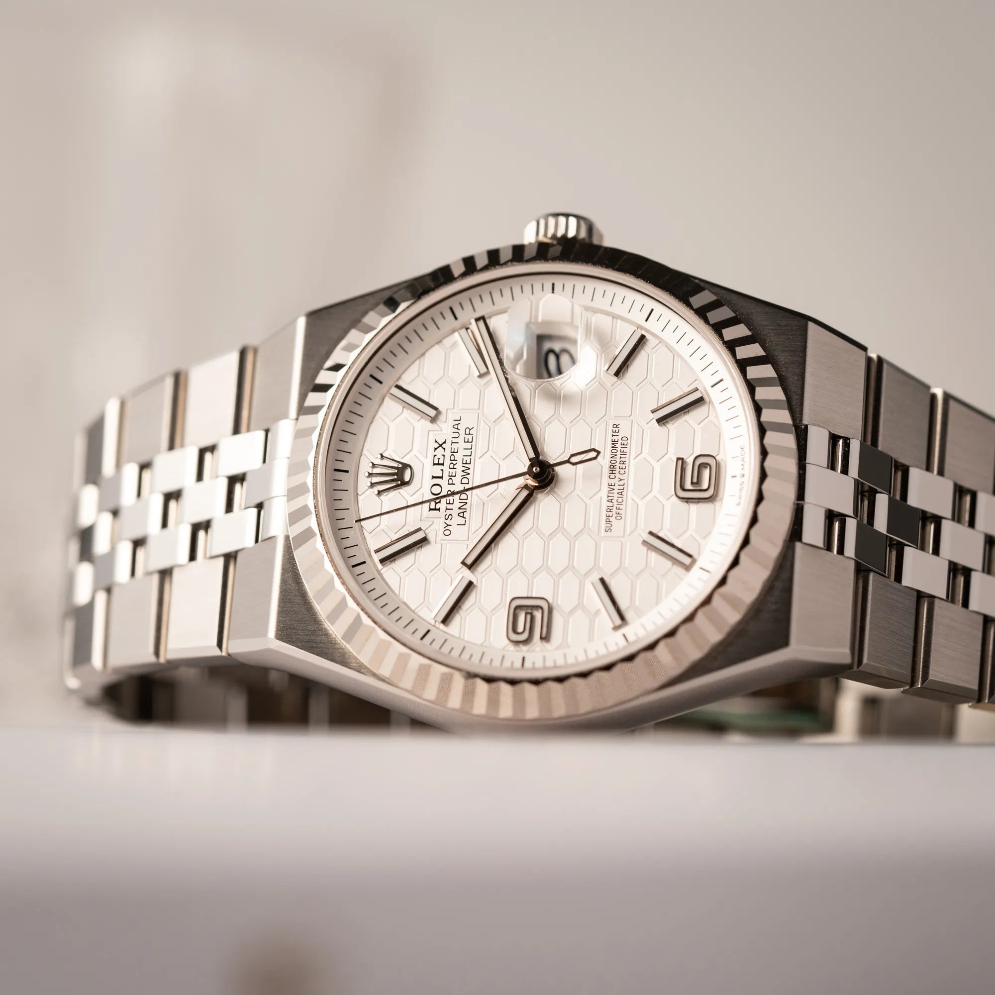Rolex Land-Dweller 40 der Referenz 127334 im neuwertigen Zustand mit dem weißen Zifferblatt in Waben-Struktur am neuen Flat-Jubilee-Armband liegt auf der seitlichen Gehäuseflanke
