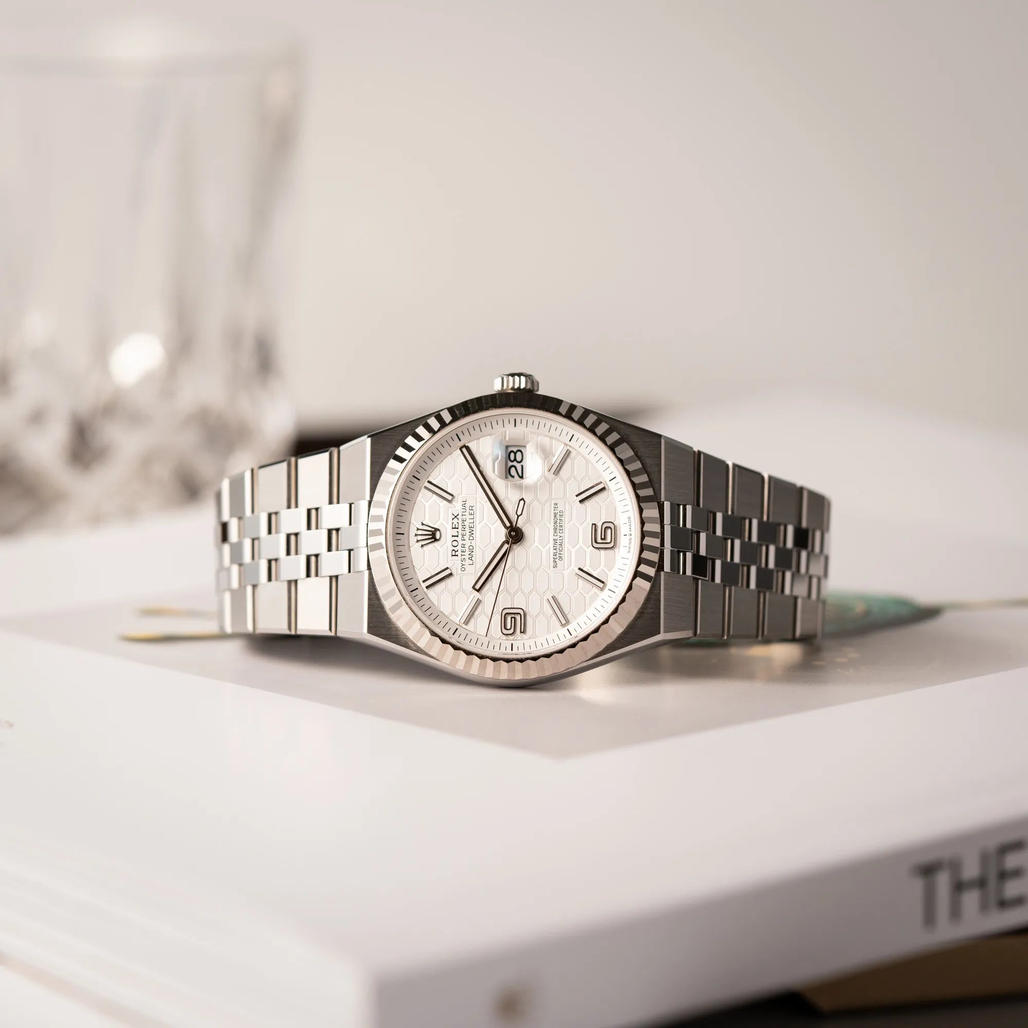 Rolex Land-Dweller 40 der Referenz 127334 im neuwertigen Zustand mit dem weißen Zifferblatt in Waben-Struktur am neuen Flat-Jubilee-Armband liegt mit der seitlichen Gehäuseflanke auf einem Rolex-Magazin