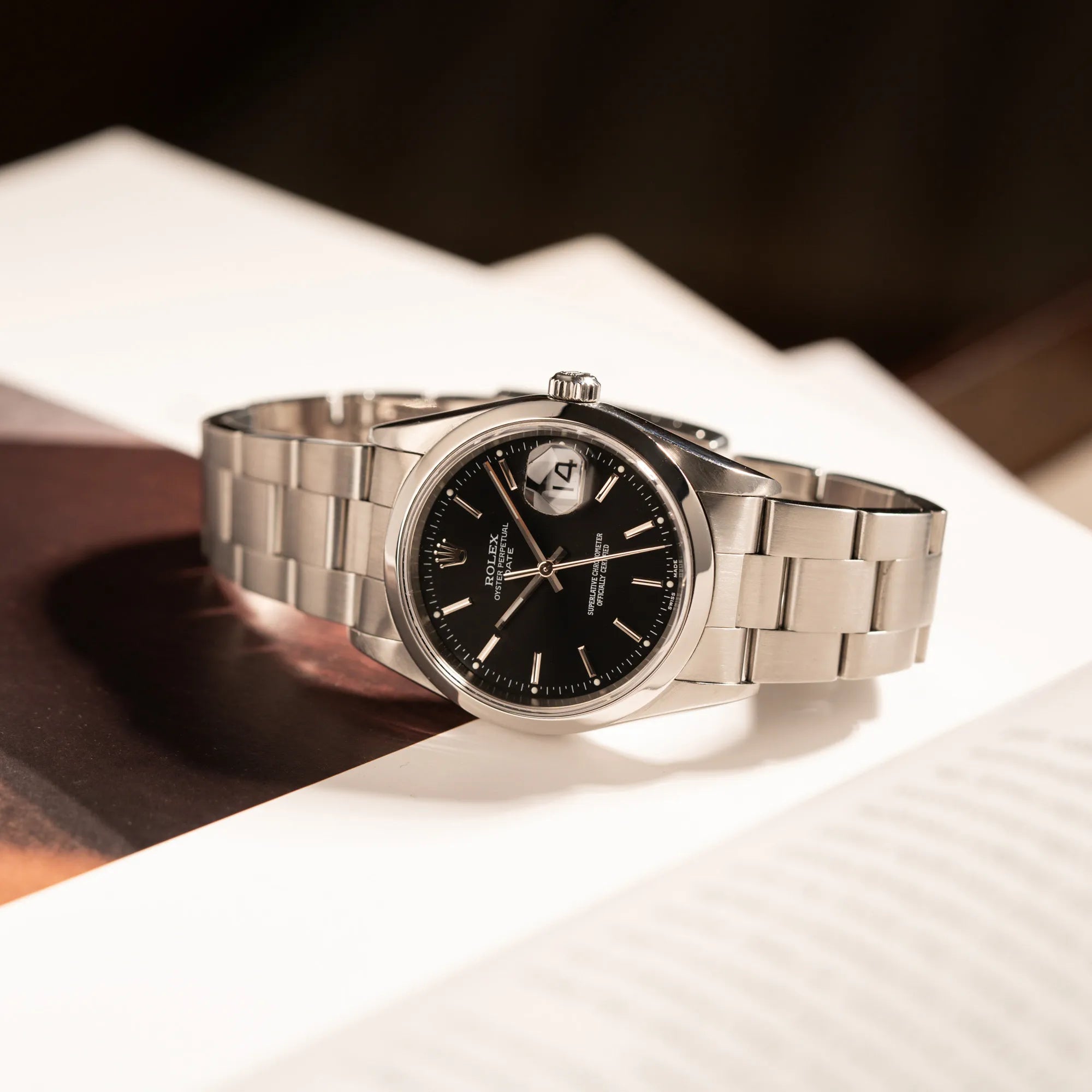 Rolex Oyster Perpetual 34 mit schwarzem Zifferblatt der Referenz 15200 mit glatter Lünette und 34mm Gehäusedurchmesser liegt seitlich auf dem Uhrengehäuse