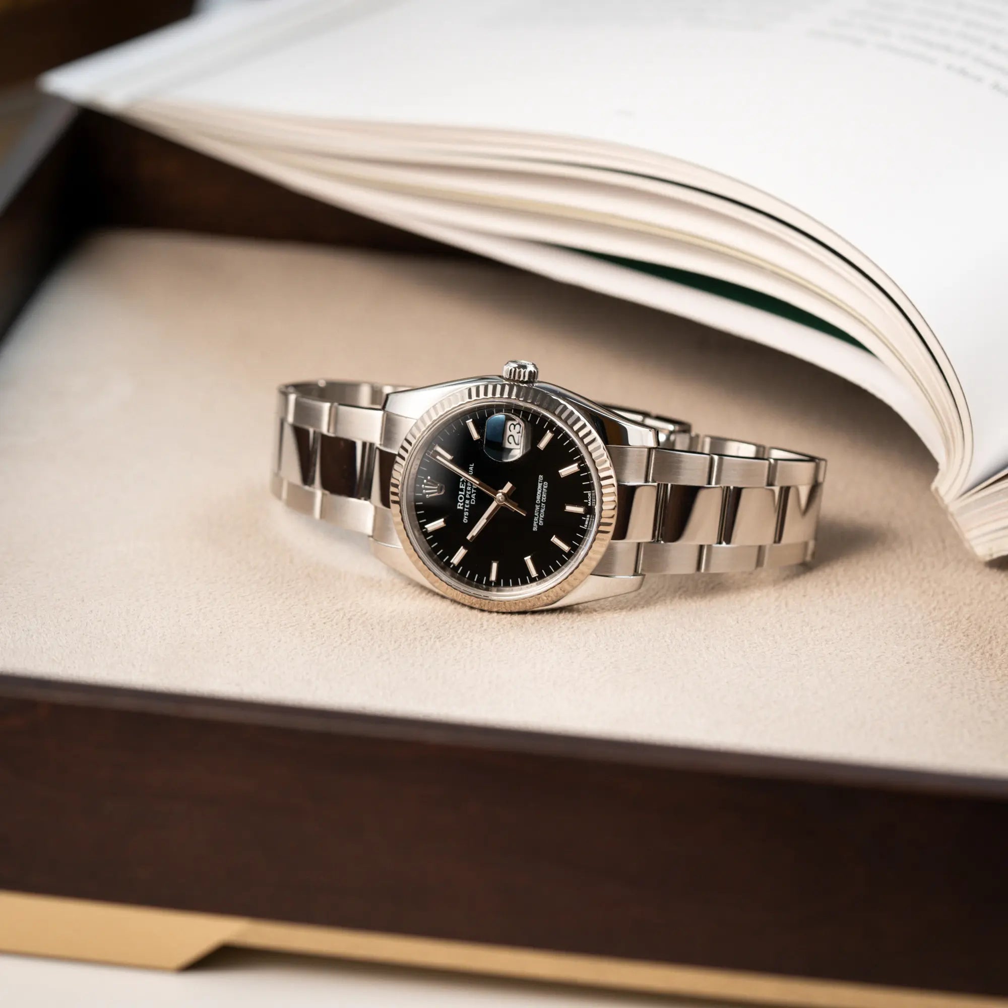 Produktfotografie als Titelbild für die Rolex Oyster Perpetual Date 34 der Referenz 115234 mit schwarzem Zifferblatt und der geriffelten Weißgold-Lünette 