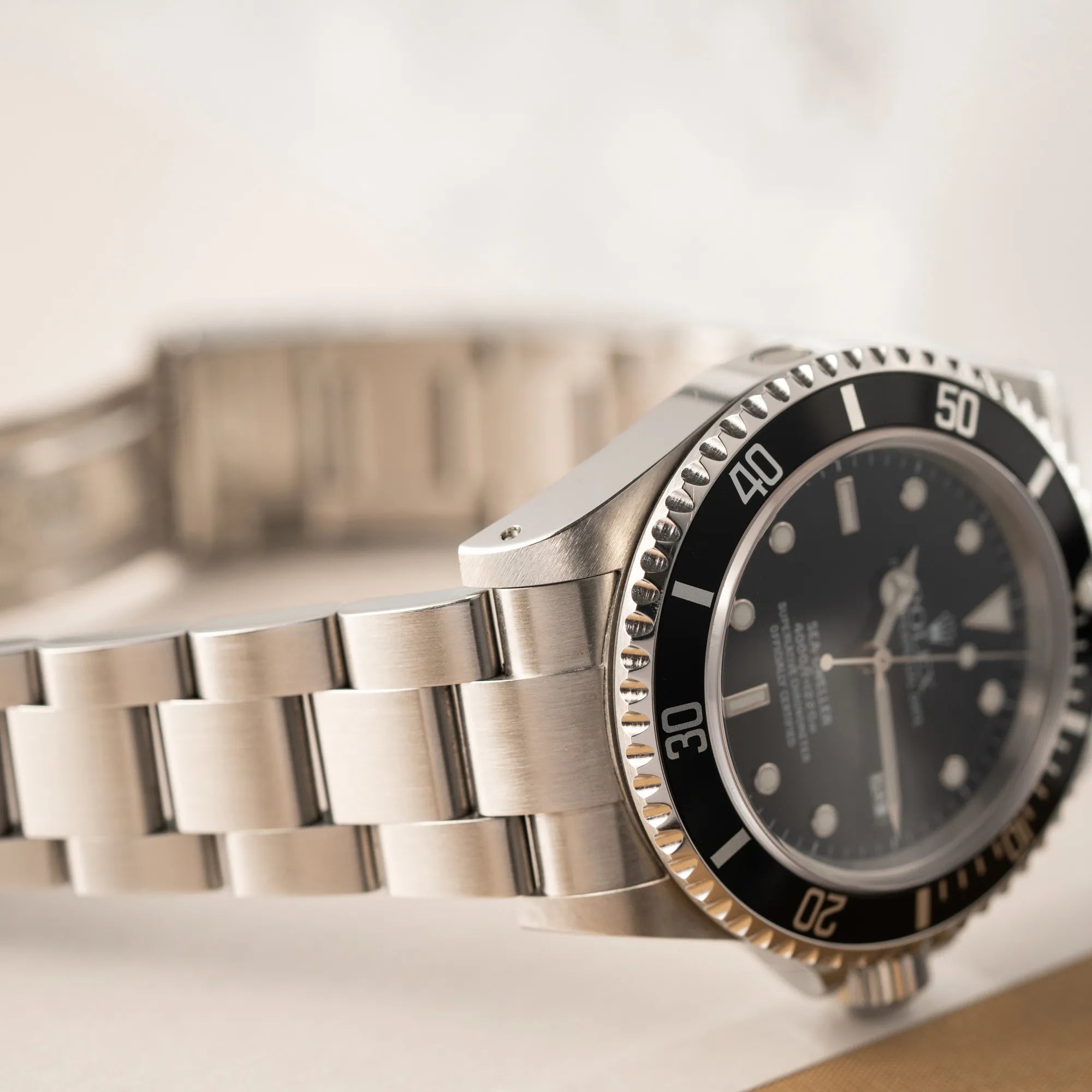 Produktfotografie der Rolex Sea-Dweller  mit schwarzem Zifferblatt und schwarzer Aluminium-Lünetten-Einlage der Referenz 16600 aus 2000, während die Uhr auf der Aufzugskrone aufliegt