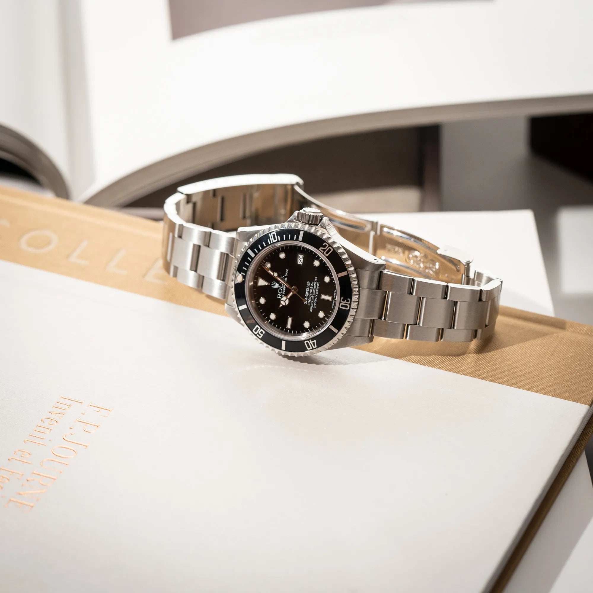 Produktfotografie der auf einem Buch liegenden Rolex Sea-Dweller 4000 der Referenz 16600 mit der klassischen schwarzen Aluminium-Lünette aus Dezember 2002