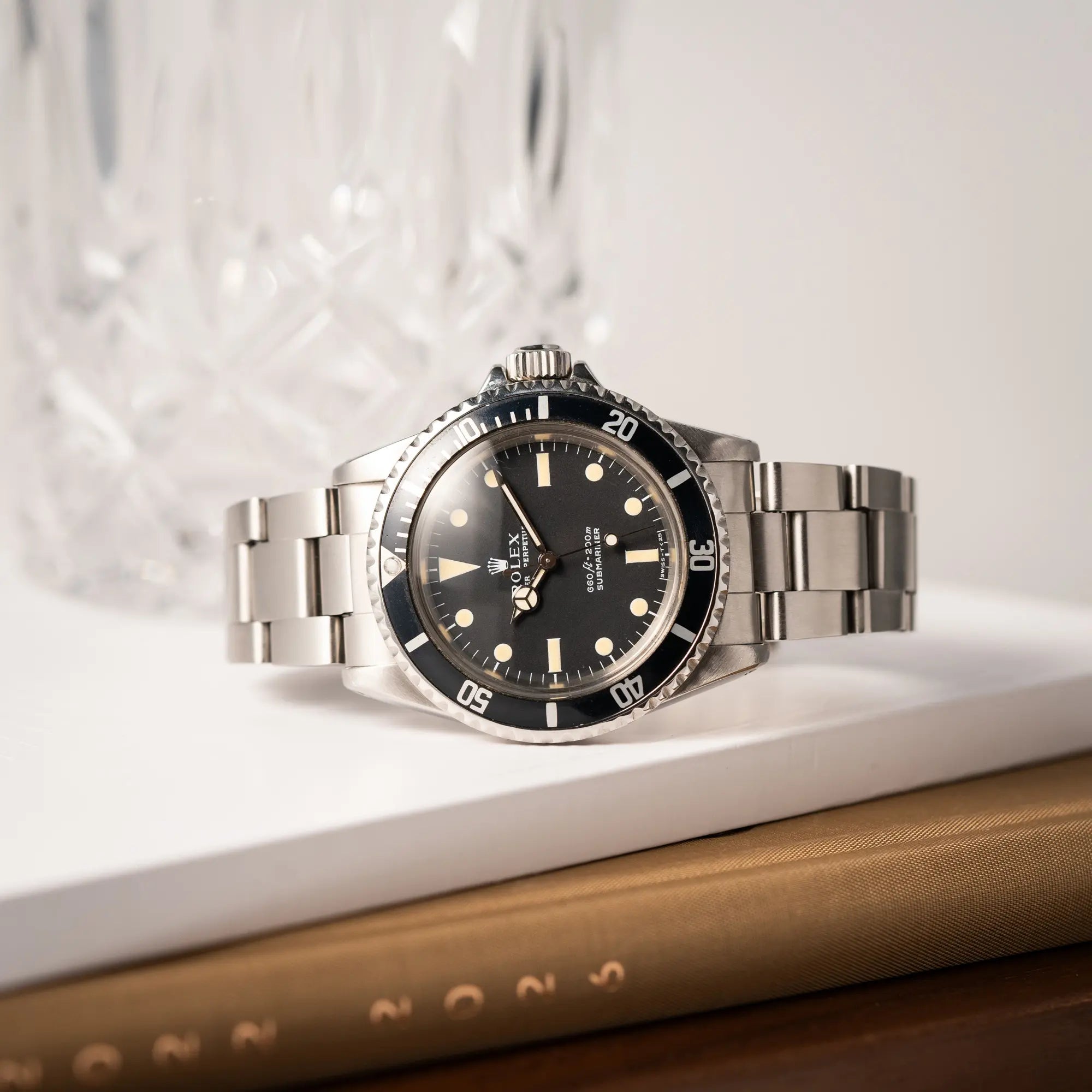 Produktfotografie der Rolex Submariner No Date MKII mit Serif Zifferblatt der Referenz 5513 aus 1970 mit gleichmäßiger Patina während ei Uhr auf der seitlichen Gehäuseflanke liegt