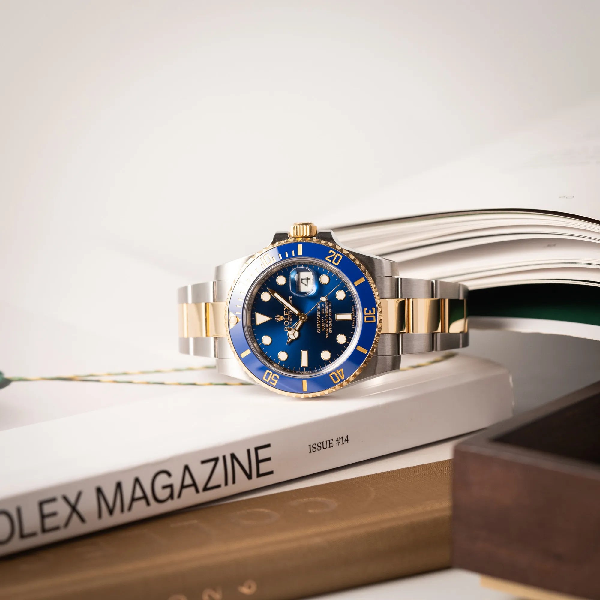Produktfotografie der Rolex Submariner Date der Referenz 116613LB in Stahl-Gold mit blauem Zifferblatt - auch mit Nickname Bluesy bennant - am passenden Oytser-Armband in Stahl-Gold zusammen mit Uhrenbüchern