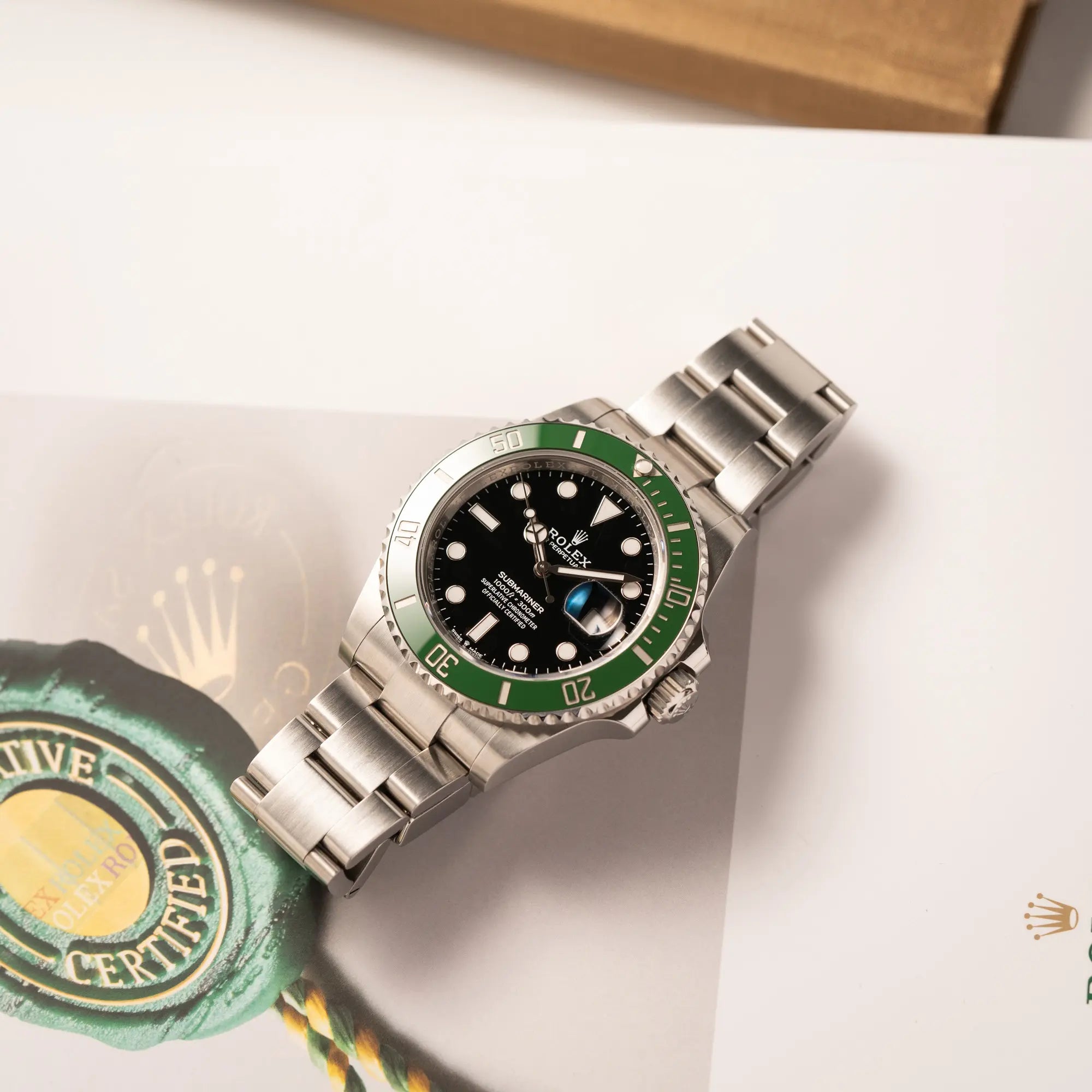 Rolex Submariner Date 126610LV, Nickname "Starbucks", mit schwarzem Zifferblatt und grüner Keramik-Lünette in der MK2-Ausführung am Oyster-Stahl-Band leigt flach auf einem Rolex-Buch