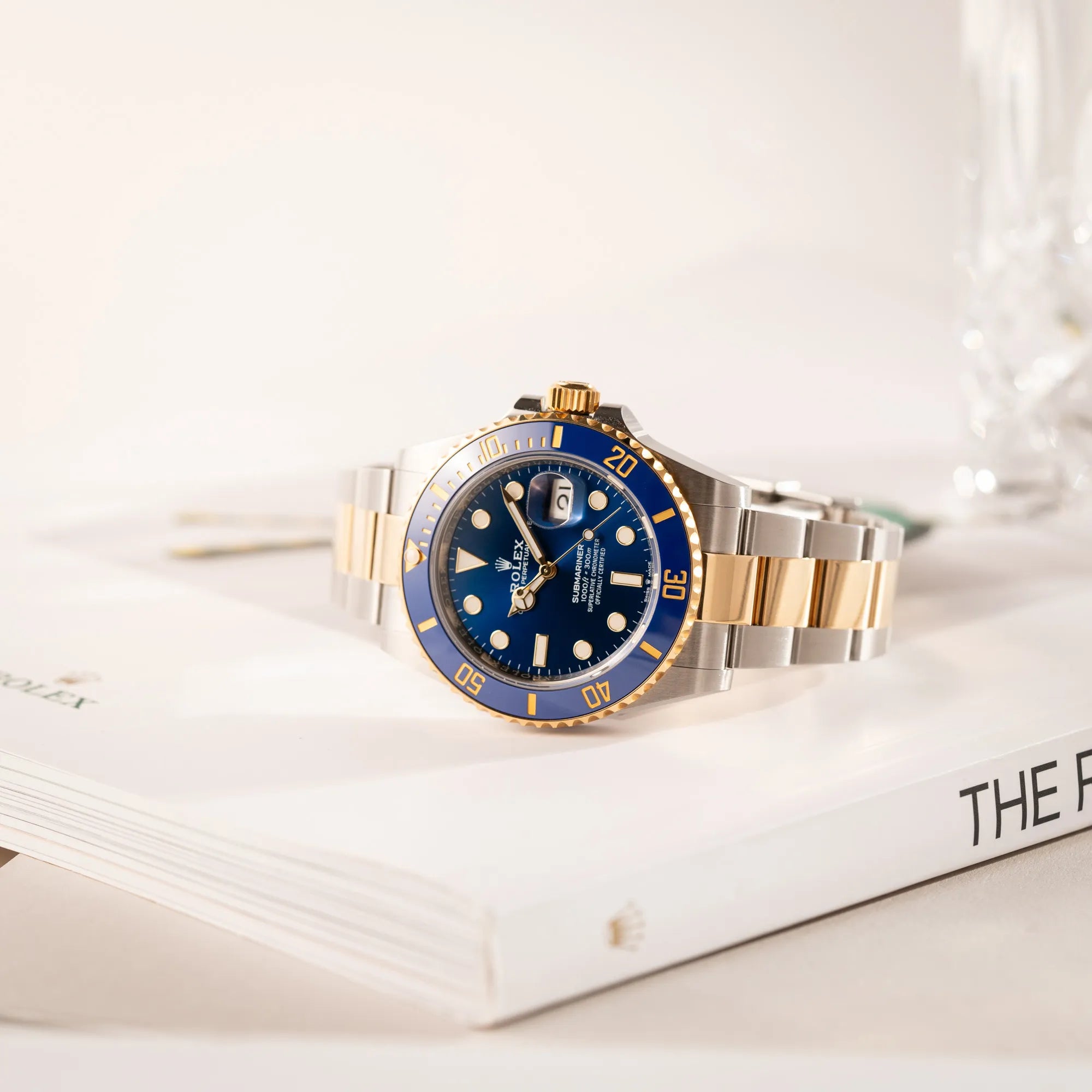 Rolex Submariner Date 126613LB Bluesy mit der typischen Kombination aus blauem Zifferblatt und Lünette mit dem Gehäuse und Armband aus Stahl-Gold leigt auf einem buch über Rolex Uhren
