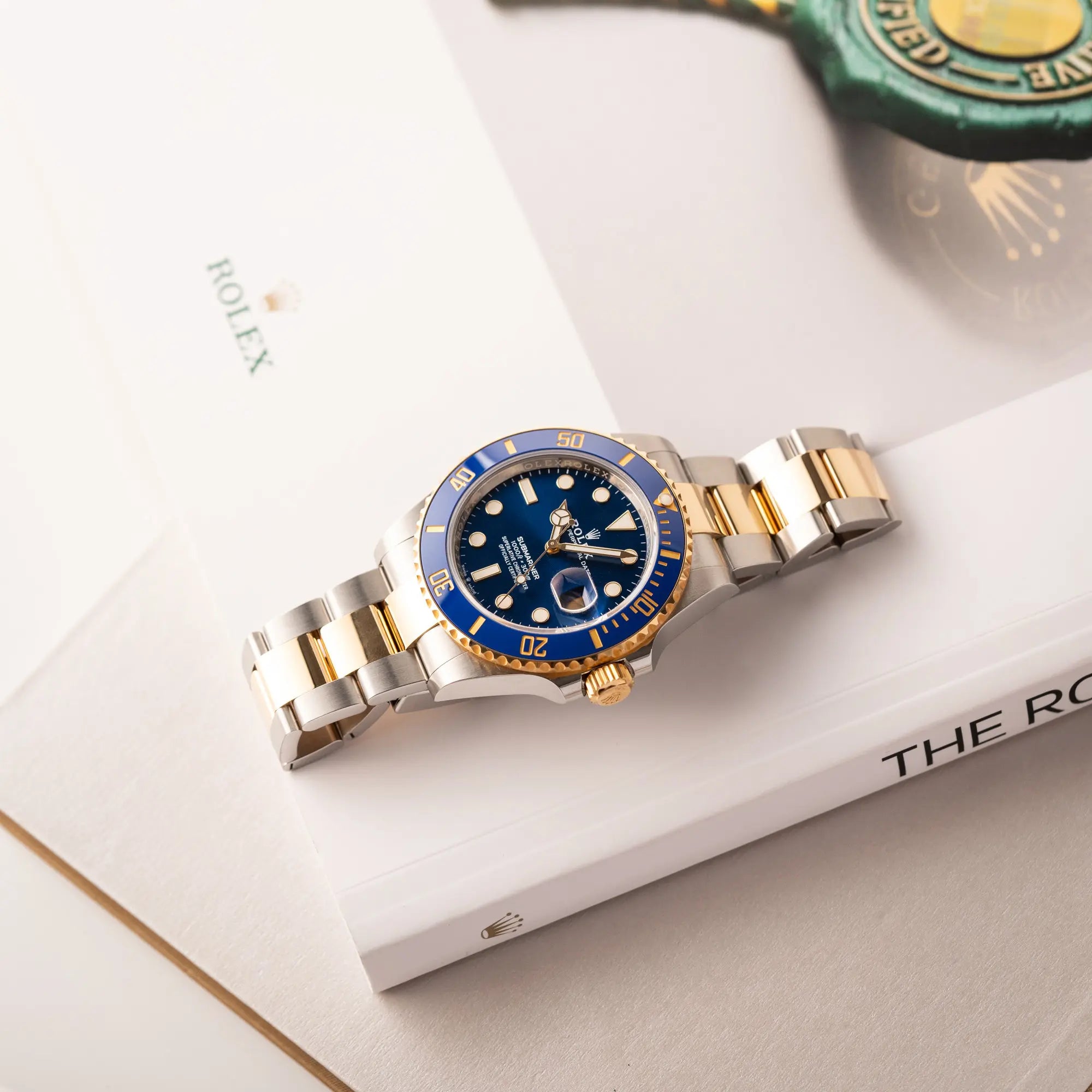 Produktfotografie zeigt die Rolex Submariner Date 126613LB Bluesy mit der typischen Kombination aus blauem Zifferblatt und Lünette mit dem Gehäuse und Armband aus Stahl-Gold flach auf einem Uhrenbuch liegend