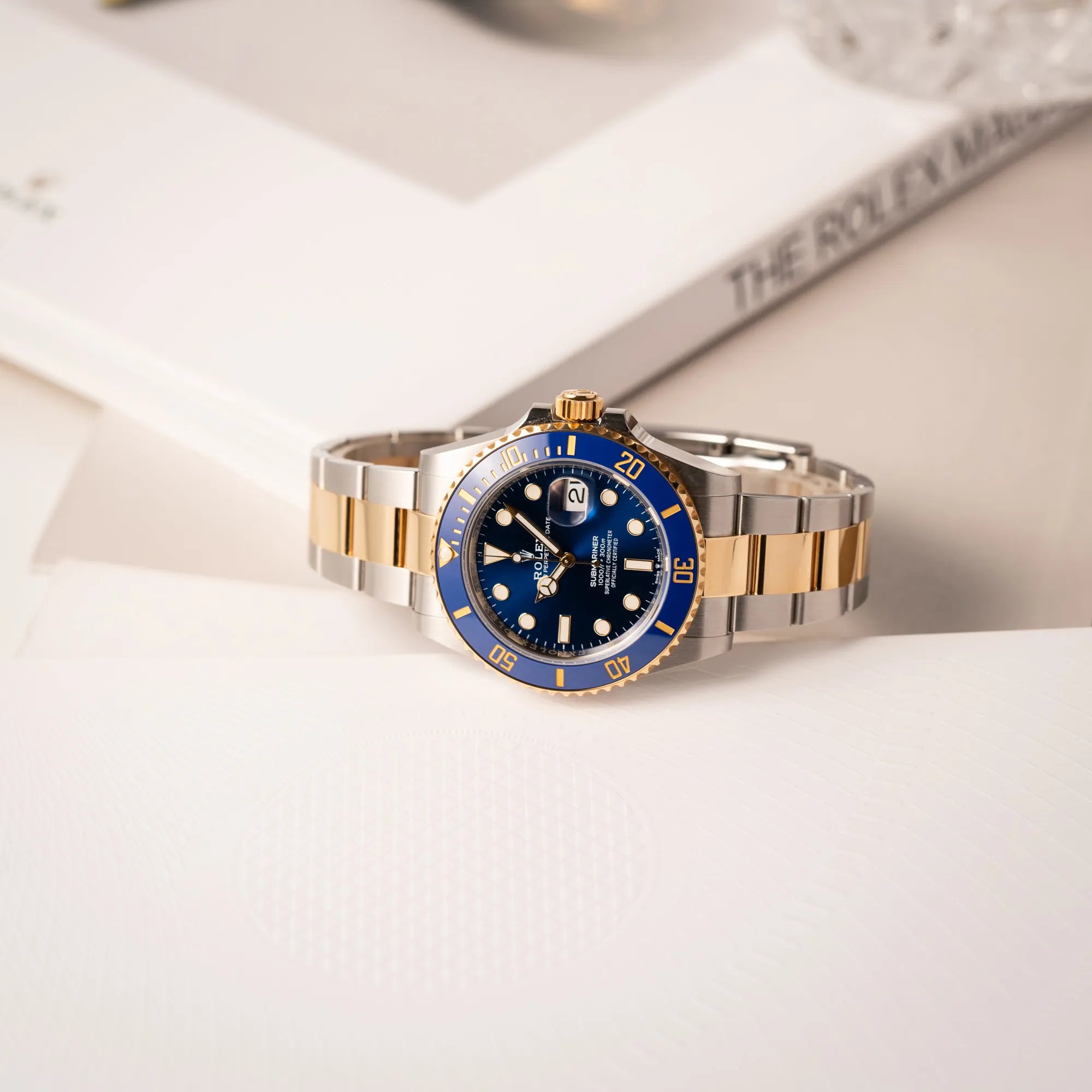Rolex Submariner Date 126613LB Bluesy mit der typischen Kombination aus blauem Zifferblatt und Lünette mit dem Gehäuse und Armband aus Stahl-Gold liegt seitlich auf dem Uhrengehäuse