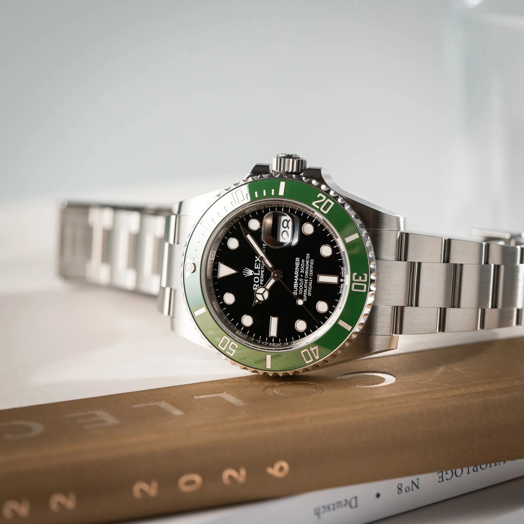 Rolex Submariner Date Starbucks 126610LV Mark 2 aus 2025 mit der typischen grünen Cerachrom-Lünette liegt seitlich auf dem Uhrengehäuse
