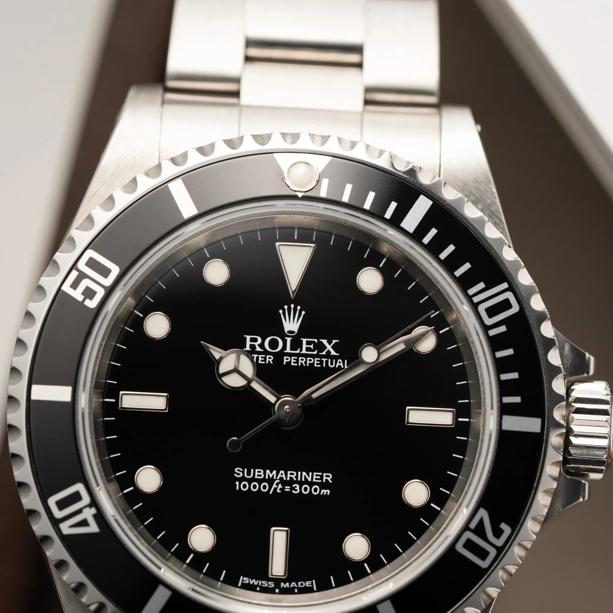 Detailaufnahme der Rolex Submariner No Date 14060M mit schwarzem Zifferblatt und der klassischen schwarzen Aluminium-Lünette mit Fokus auf dem Zeigersatz