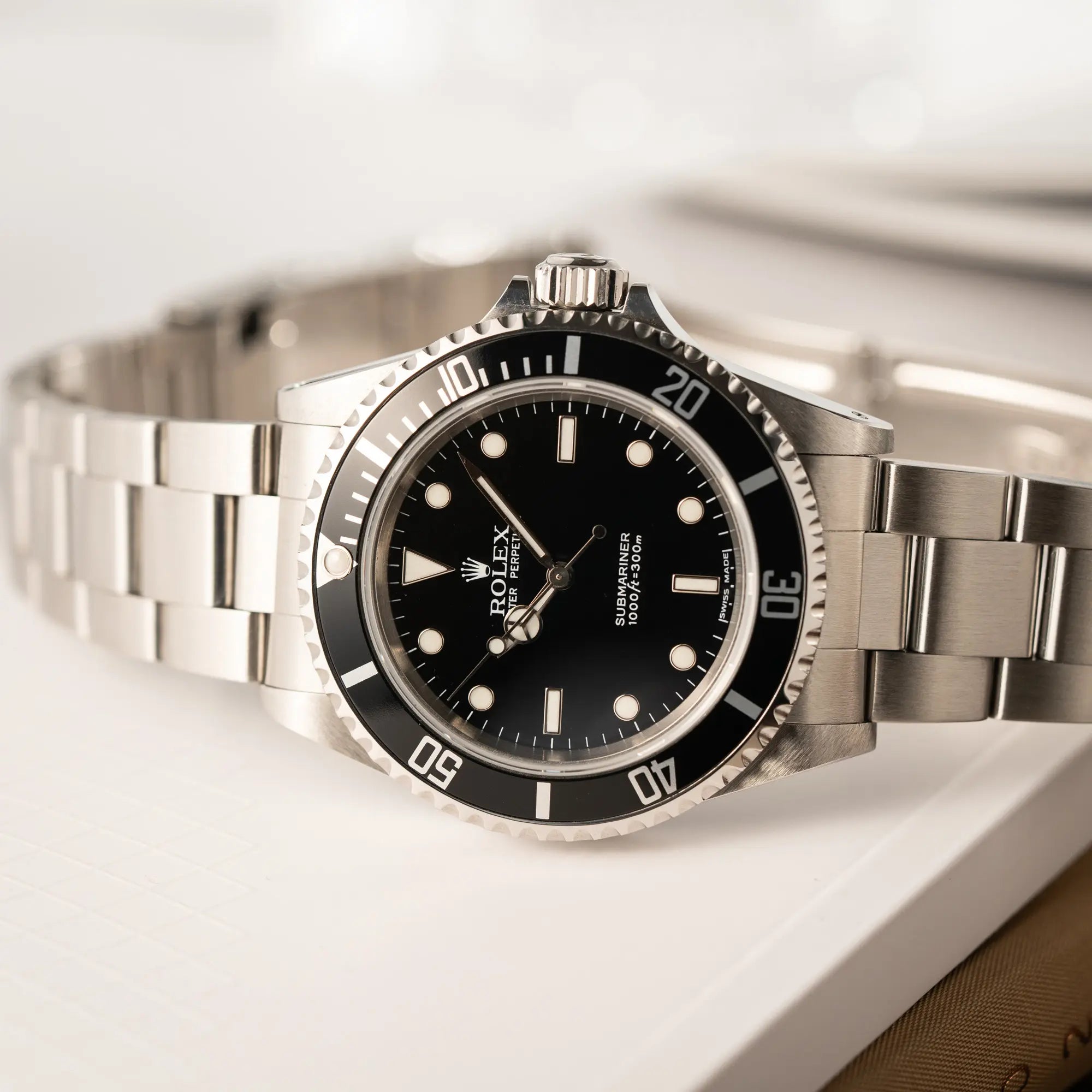 Produktfotografie der seitlich auf dem Uhrengehäuse liegenden Rolex Submariner No Date 14060M mit schwarzem Zifferblatt und der klassischen schwarzen Aluminium-Lünette