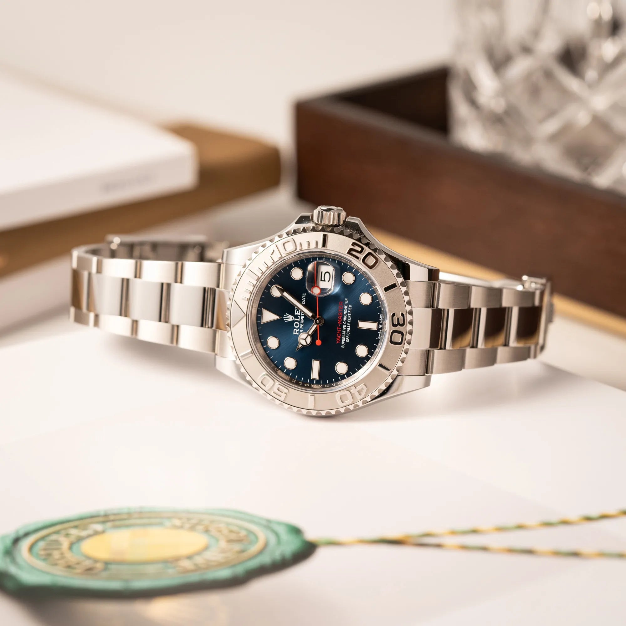 Rolex Yacht-Master 40 der Referenz 126622 mit der Platin-Lünette in der blauen Zifferblatt-Variante liegt seitlich auf der Gehäuseflanke auf einem Buch über Rolex-Logo