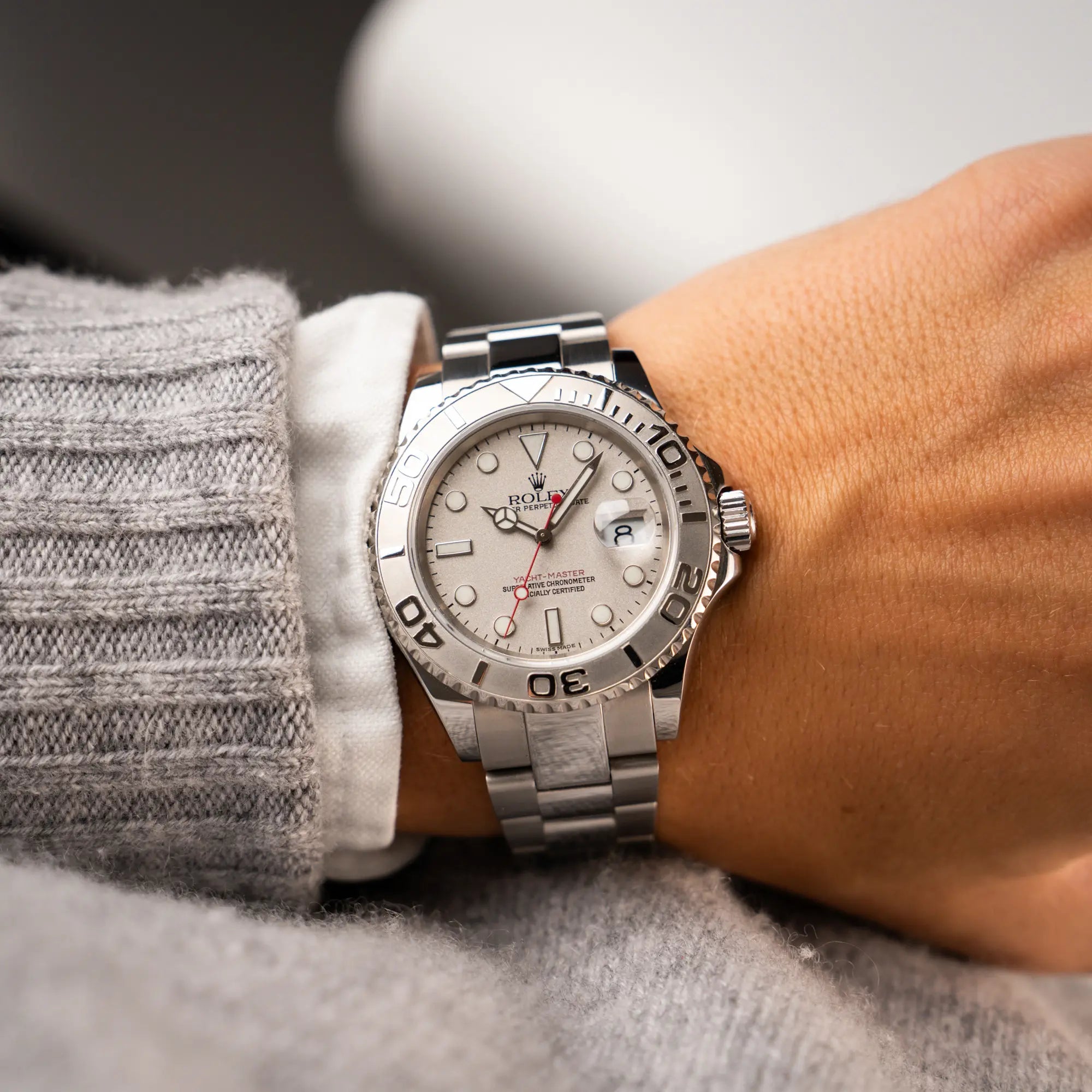 Wristshot eines Mannes in grauem Strickpullover, der die Rolex Yacht-Master 40 Rolesium der Referenz 16622 mit dem silberfarbenen Platin-Zifferblatt und Platin-Lünette, sowie einem auffälligen in Rot gehaltenen Sekundenzeiger, trägt
