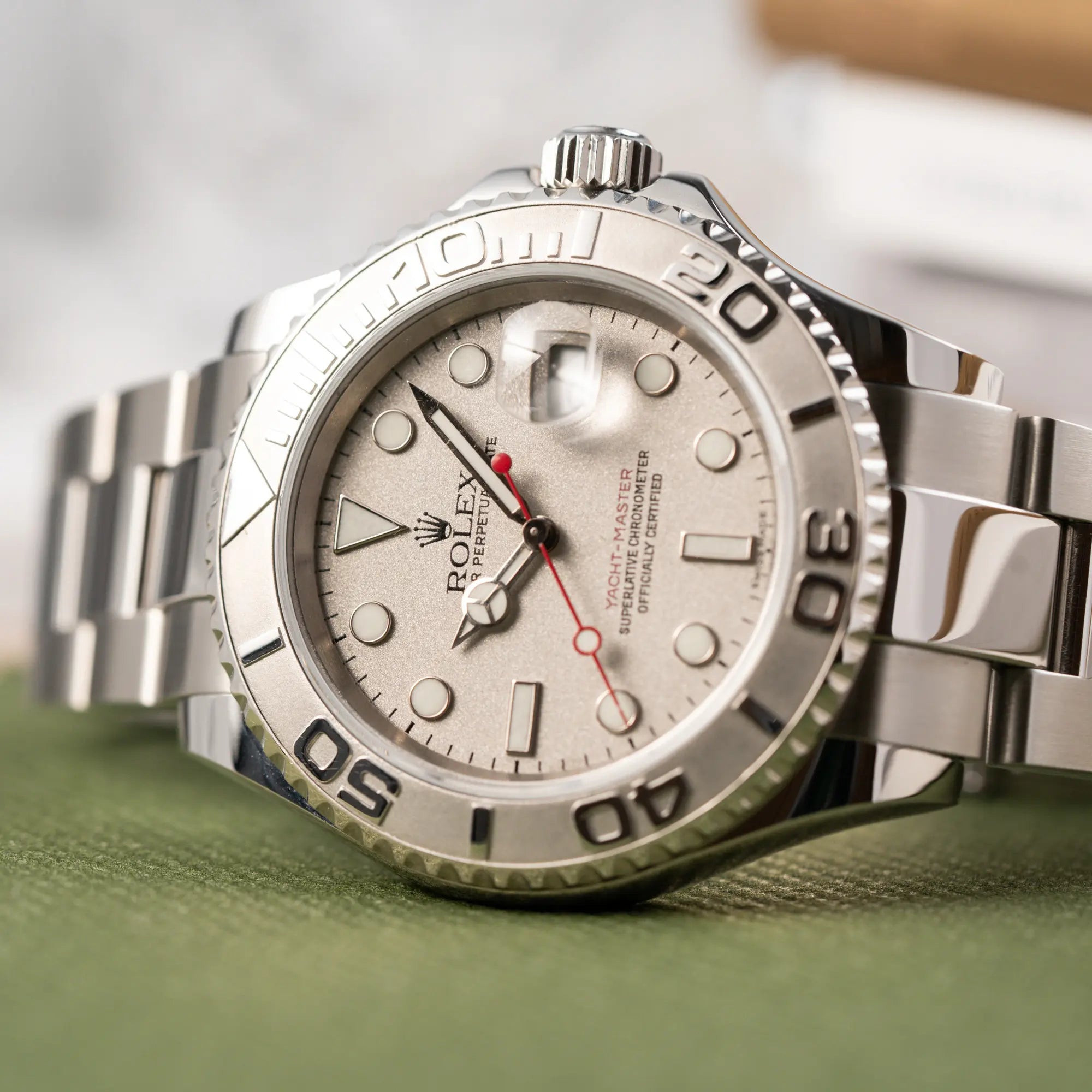 Nahaufnahme der seitlich auf dem Gehäuse liegenden Rolex Yacht-Master 40 Rolesium der Referenz 16622 mit dem silberfarbenen Platin-Zifferblatt und Platin-Lünette, sowie einem auffälligen in Rot gehaltenen Sekundenzeiger 