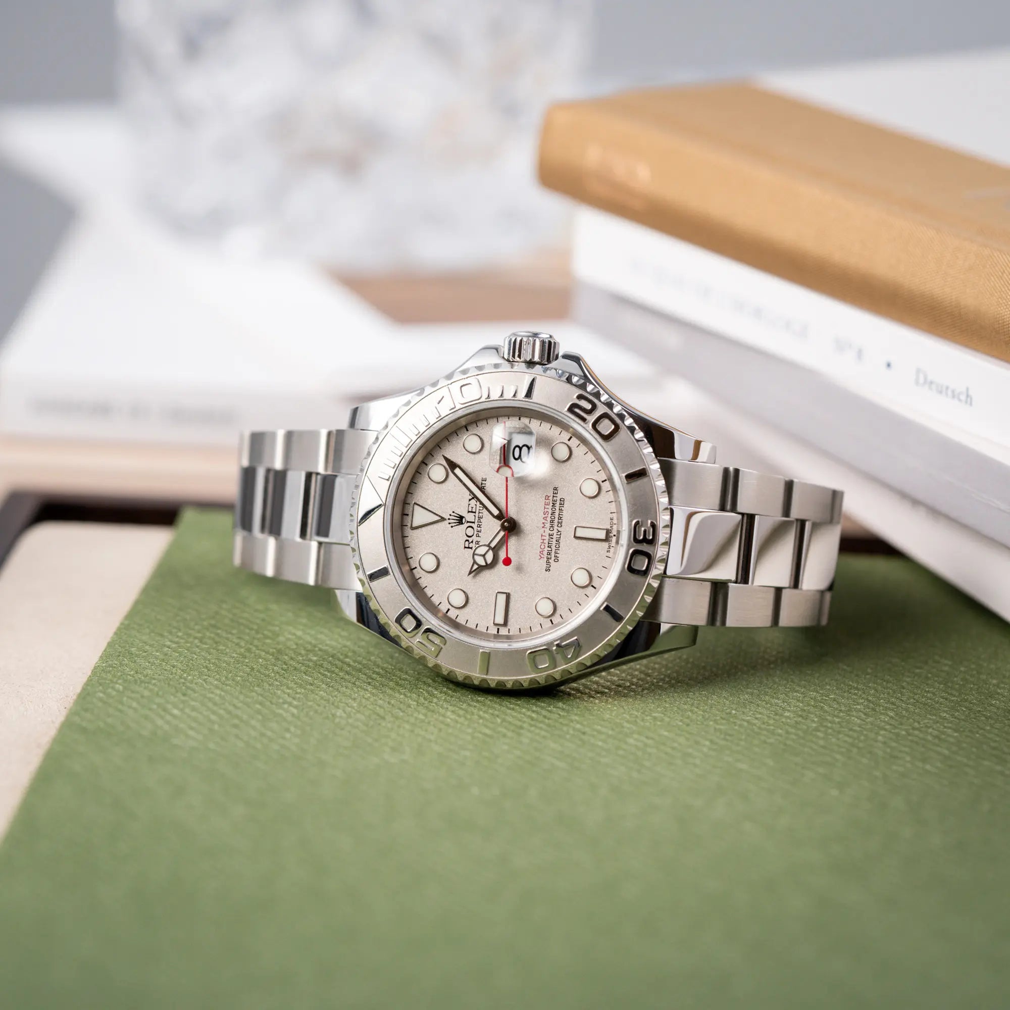 Produktfotografie der seitlich auf dem Uhrengehäuse liegenden Rolex Yacht-Master 40 Rolesium der Referenz 16622 mit dem silberfarbenen Platin-Zifferblatt und Platin-Lünette, sowie einem auffälligen in Rot gehaltenen Sekundenzeiger 
