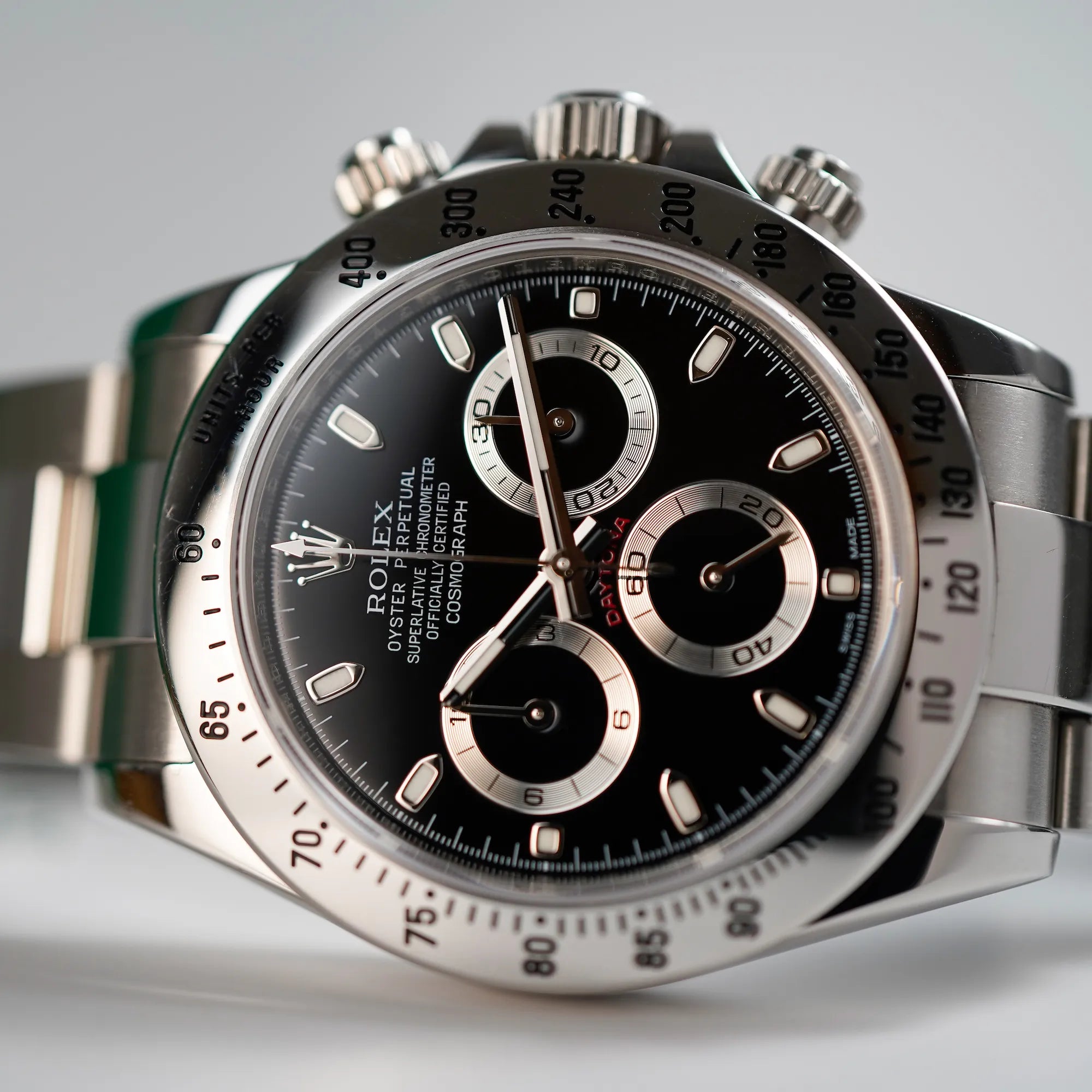 Produktfoto der auf dem seitlichen Gehäuse liegenden Rolex Cosmograph Daytona mit dem schwarzen Zifferblatt und der Edelstahl-Lünette