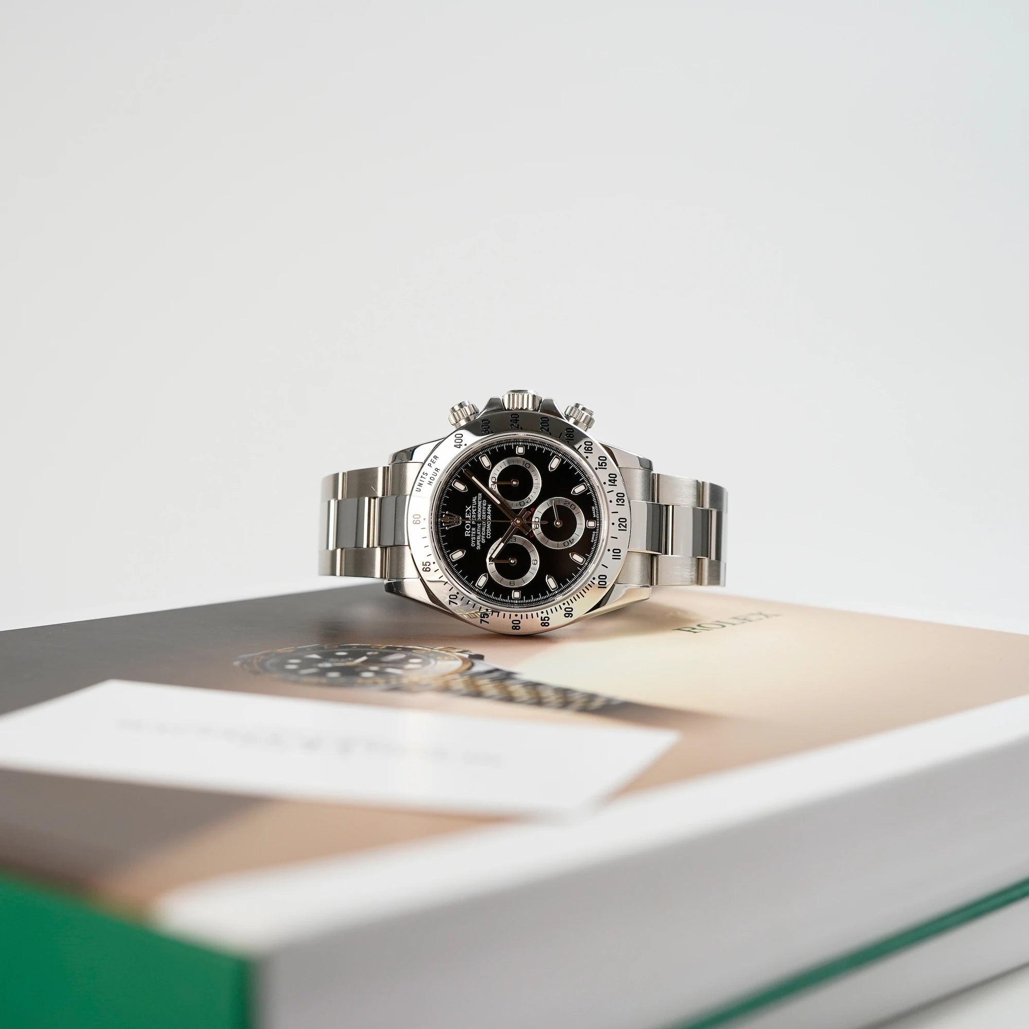 Produktfotografie der Rolex Cosmograph Daytona mit dem schwarzen Zifferblatt und der Edelstahl-Lünette, die auf dem Rolex Katalog liegt