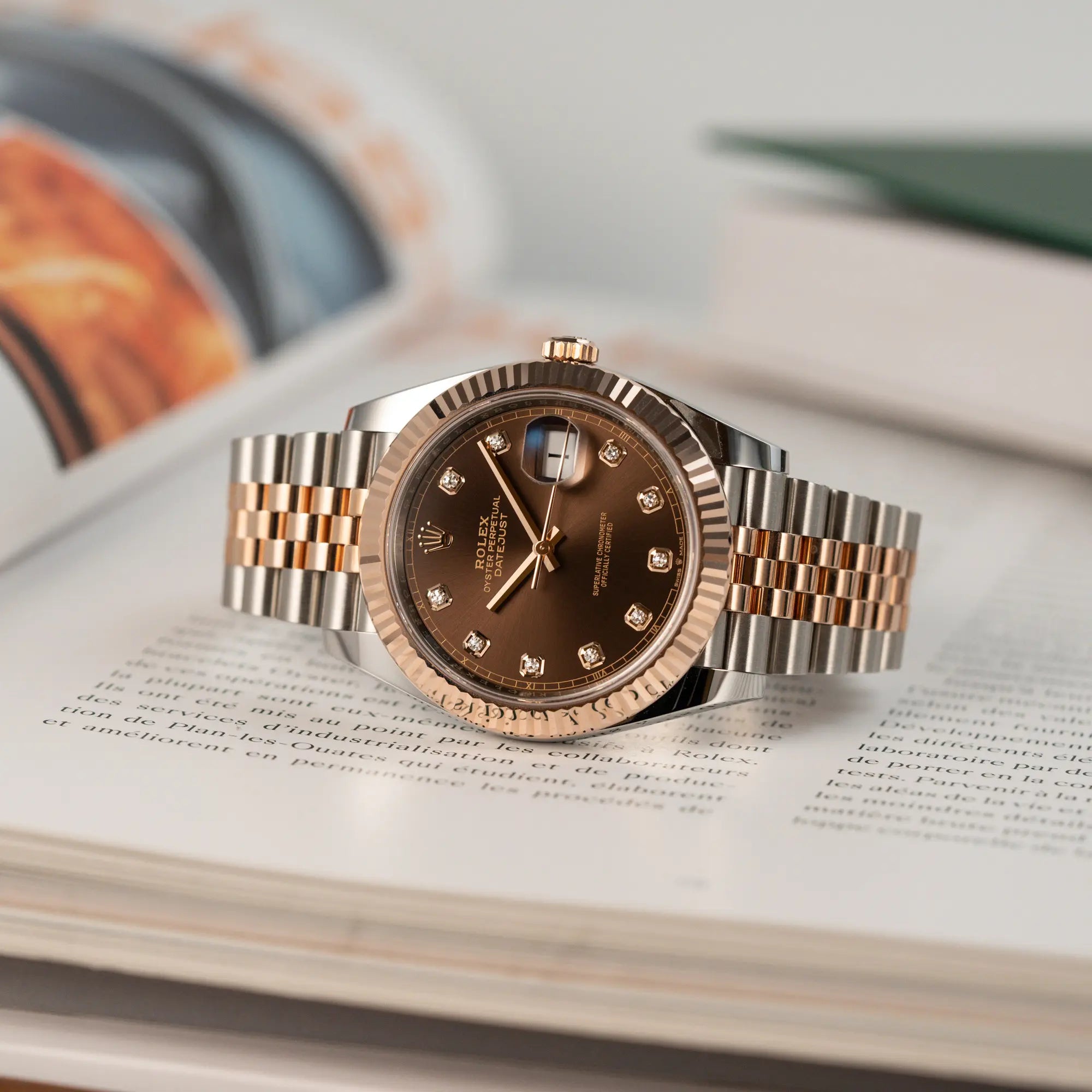 Produktfotografie der Rolex Datejust 41 in Stahl-Rosegold mit braunem Diamant-Zifferblatt, während die Uhr auf einem Buch liegt