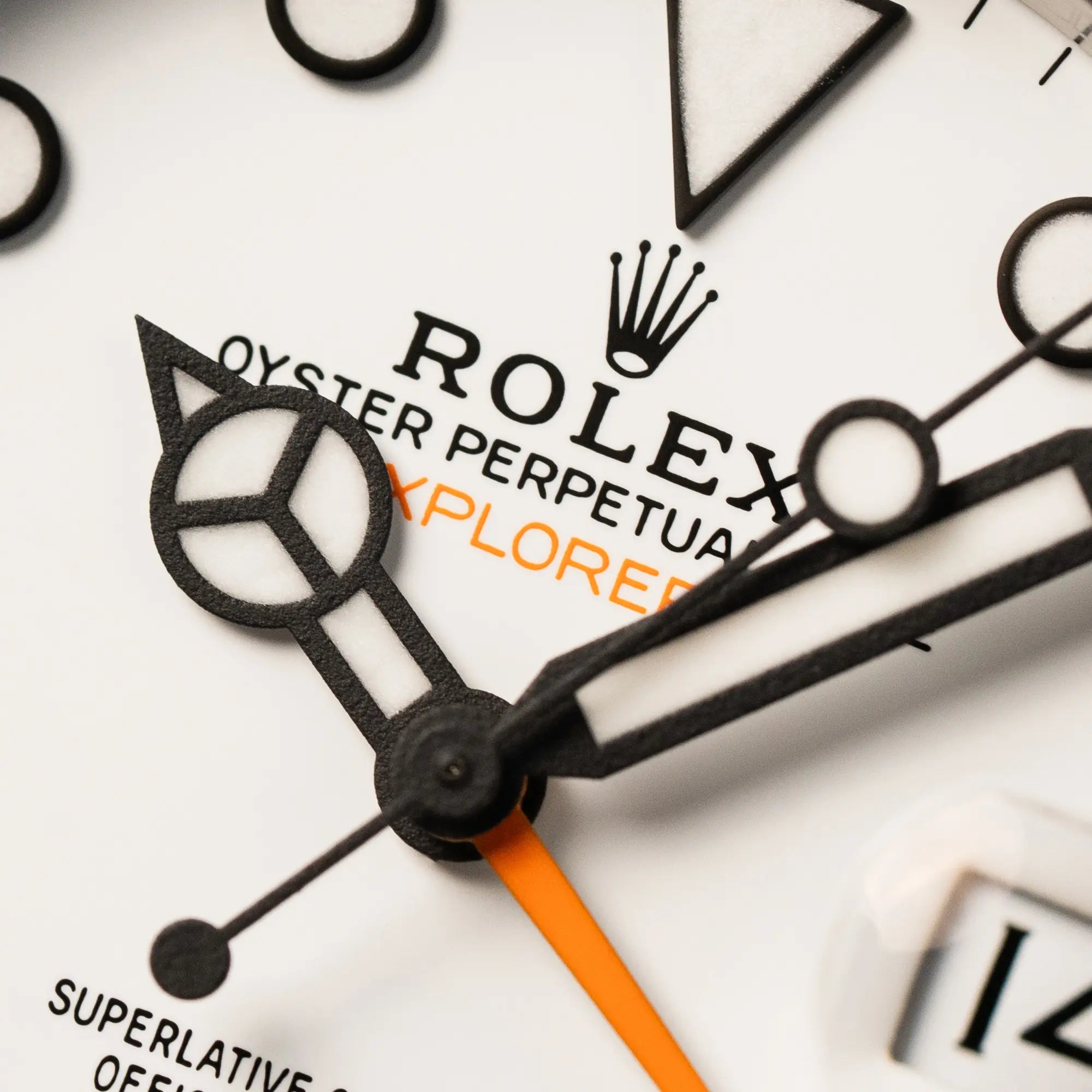 Makroaufnahme des weißen Zifferblatts mit Fokus auf dem Zeigersatz und dem "Rolex Oyster Perpetual Explorer II" Schriftzug mit orangen Akzenten