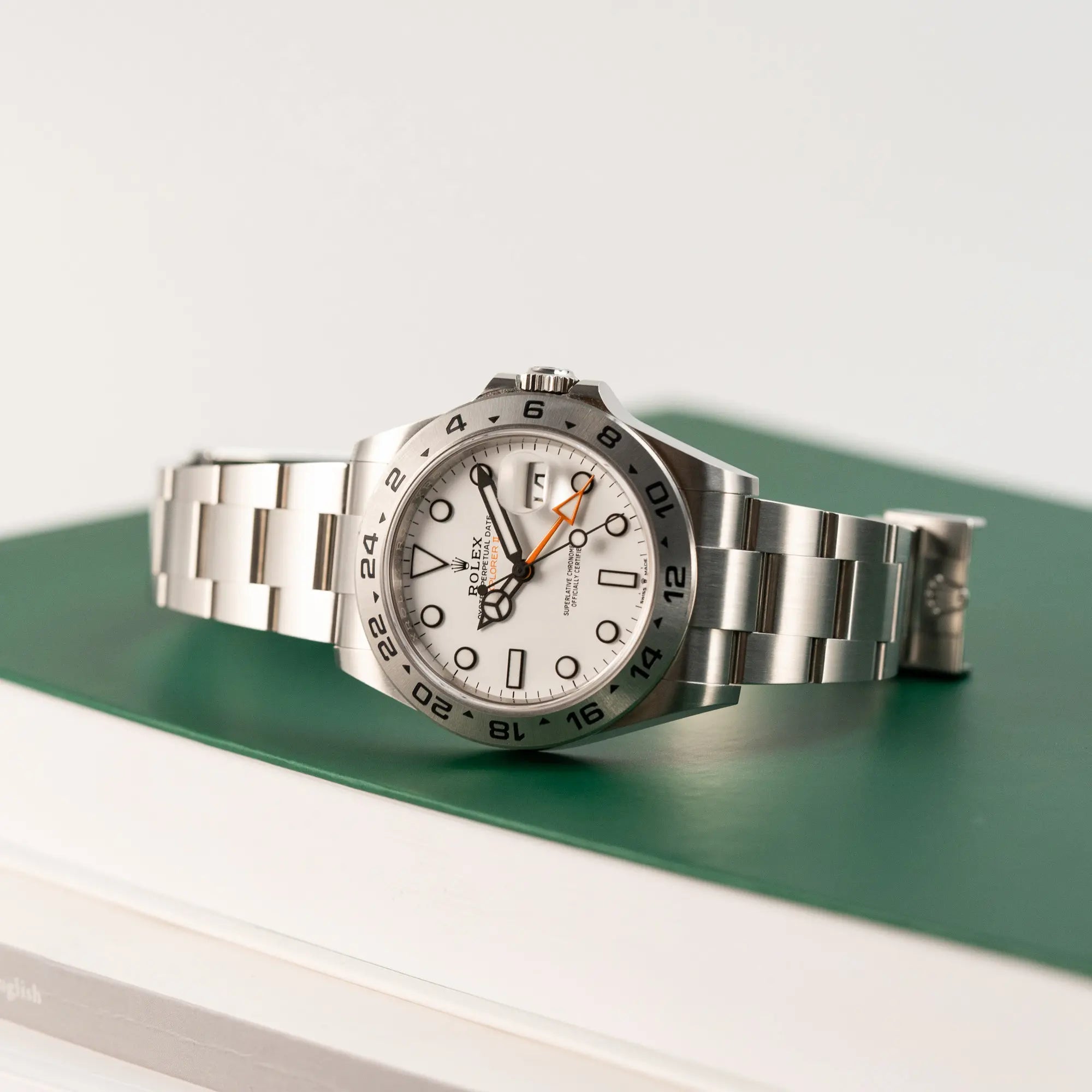 Produktfotografie der Rolex Explorer II im 42mm Oyster-Gehäuse (Referenz 226570) mit weißem Zifferblatt und orangem GMT_Zeiger, während diese auf einem rolex-typsichen grünem Buch liegt
