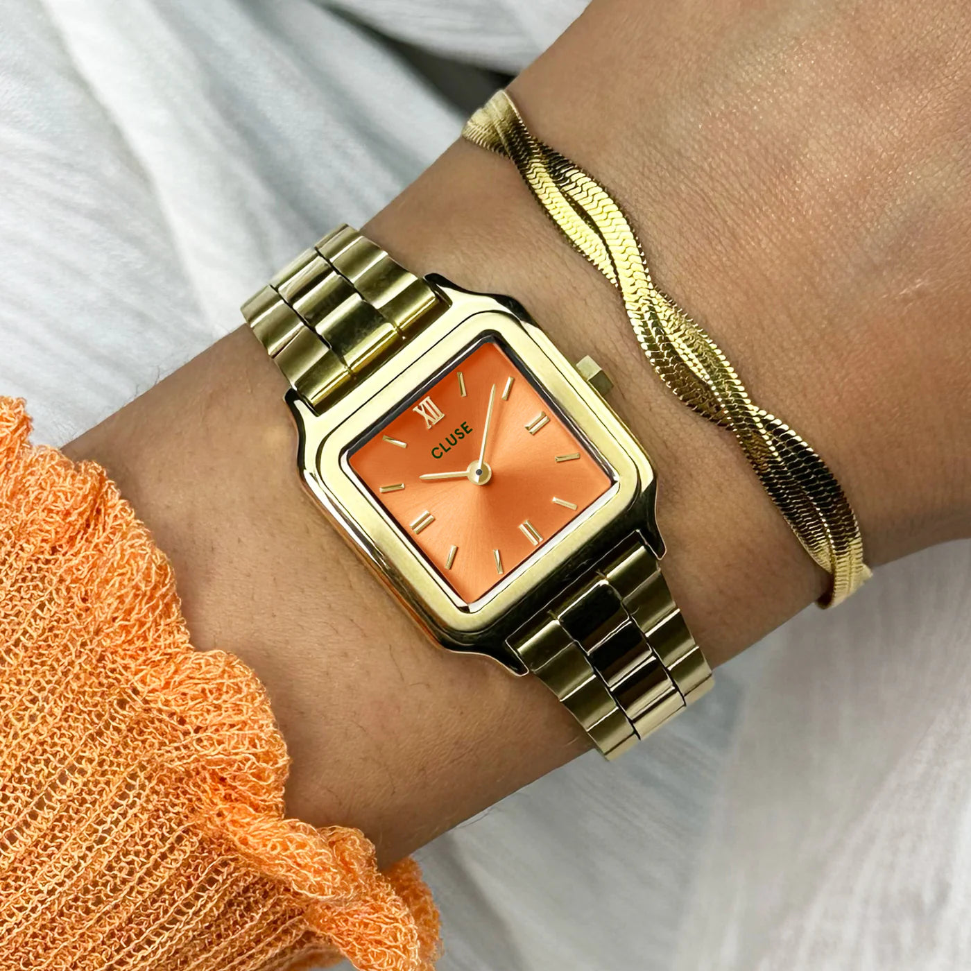 Wristshot der Cluse Stahl-Uhr "Gracieuse Petite" mit einem gelbgold-farbenem Gehäuse und orangem Zifferblatt an einem Frauenhandgelenlk
