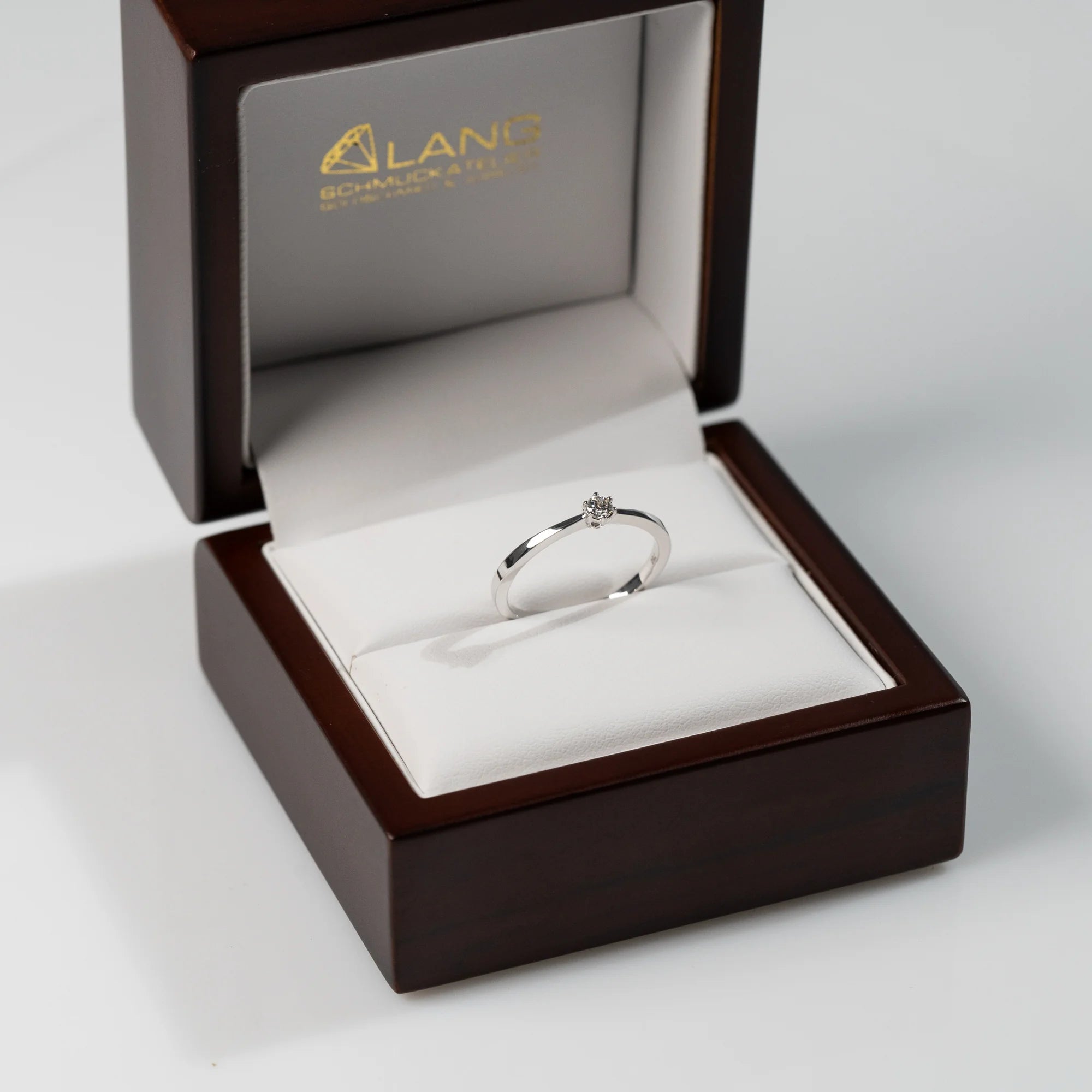 Verlobungsring "Promise" aus der Schmuckatelier Lang Collection mit einem in einer 6er Kappe gefassten Diamanten steckt in der hölzernen Schmuck-Box