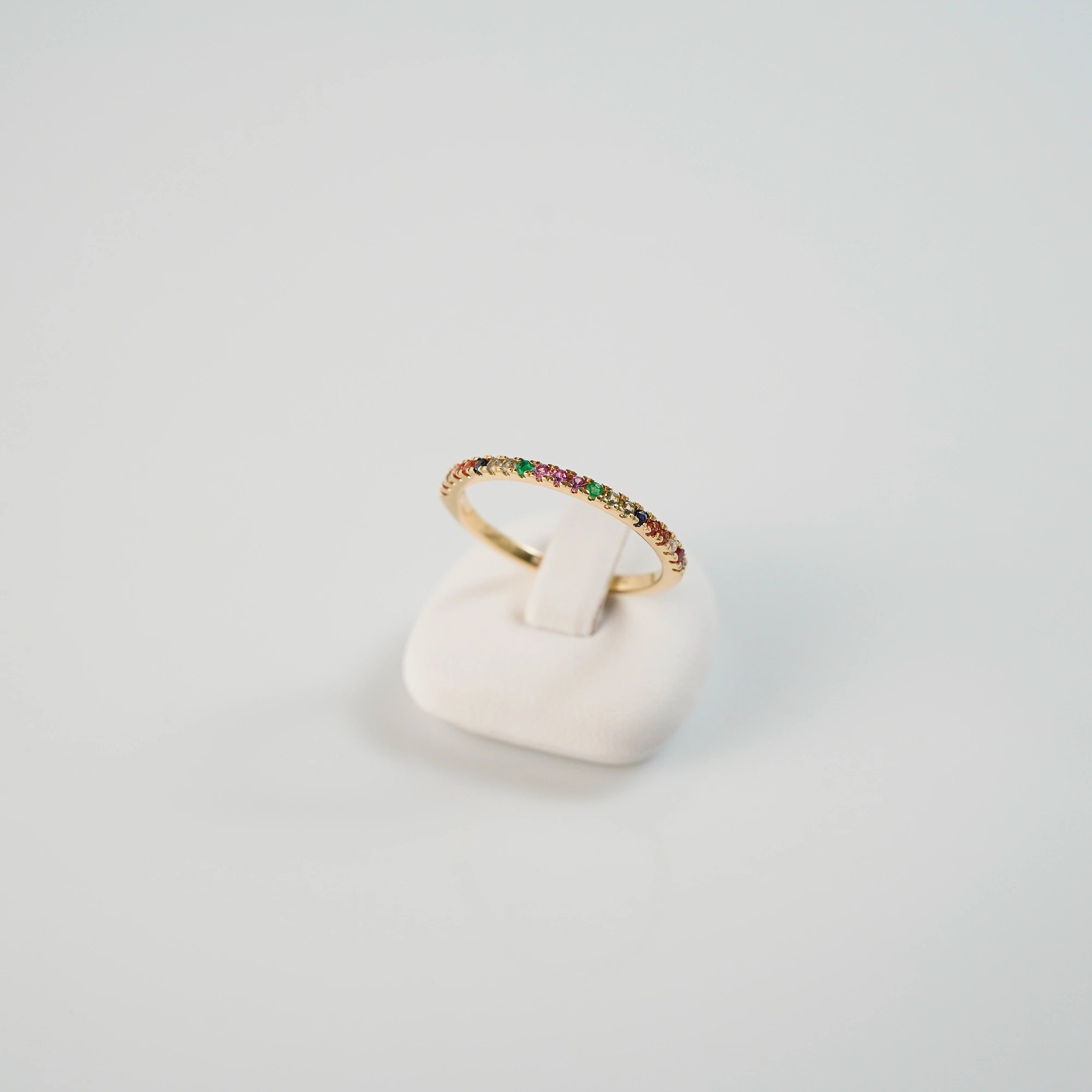 Produktfoto des liegenden Memoire-Rings mit einem Rainbow-Setting aus verschiedenen Edelsteinen mit einem bunten Farbspiel, auf einem Ringständer präsentiert