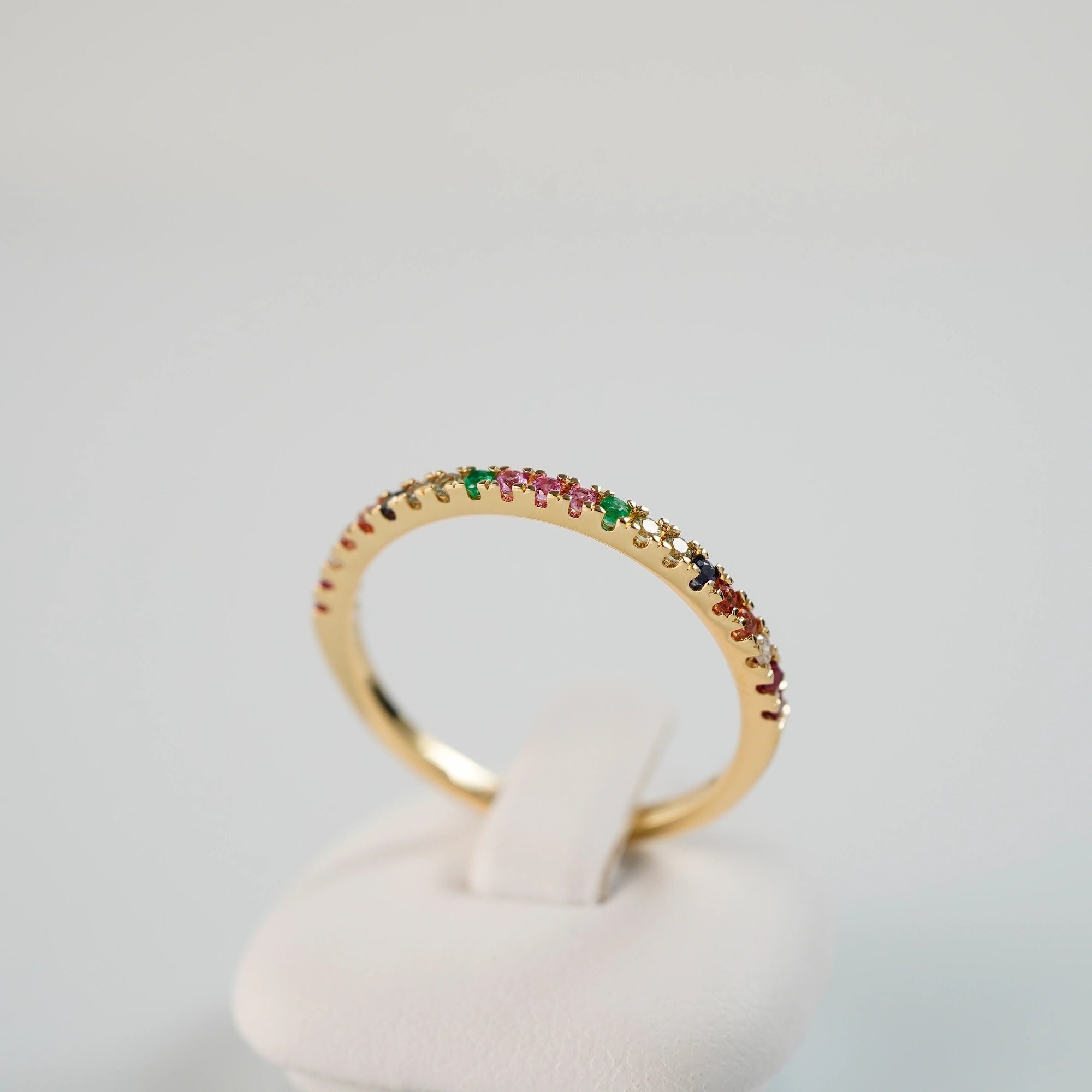 Produktfoto des liegenden Memoire-Rings mit einem Rainbow-Setting aus verschiedenen Edelsteinen mit einem bunten Farbspiel, mit Fokus auf den gefassten Edelsteinen