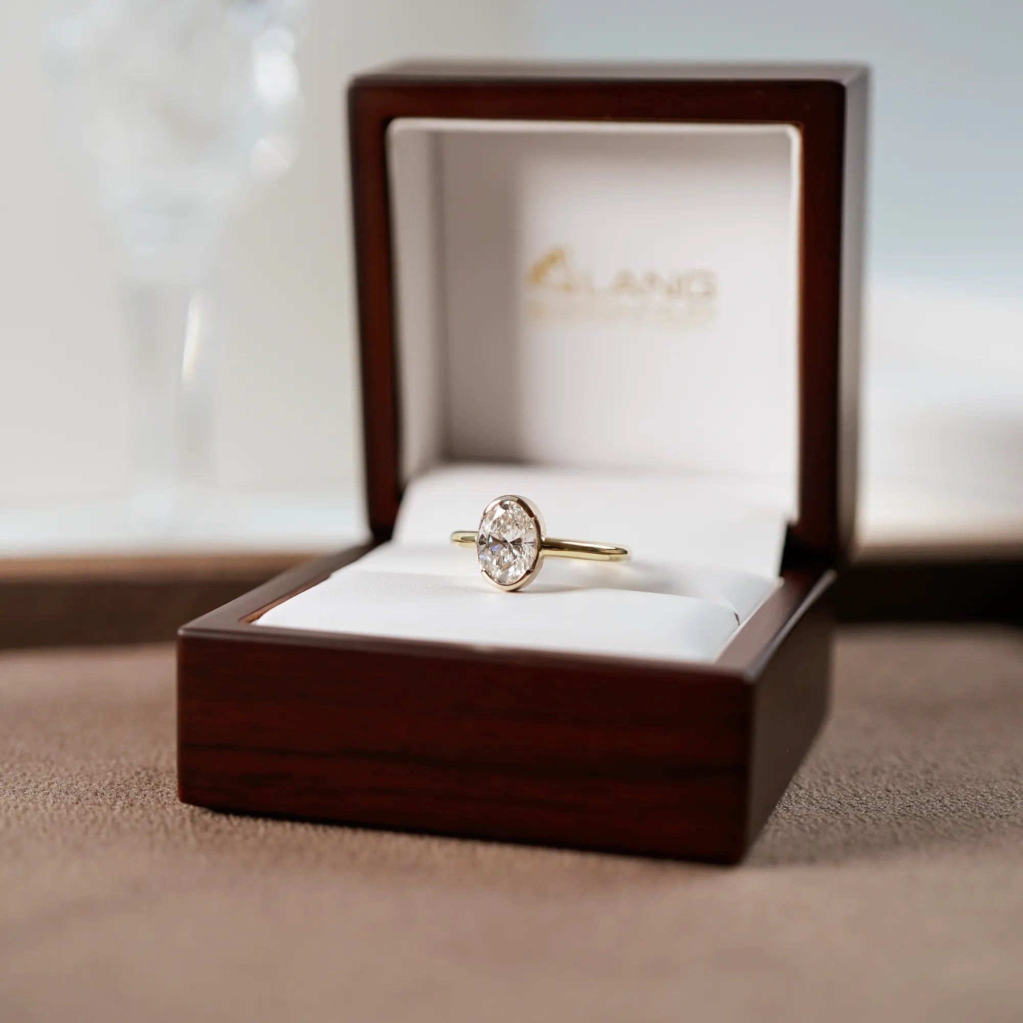 Der in Gelbgold gefertigte Verlobungsring "Gleaming Love" mit einem großen Labor-Diamanten mit 2.03ct liegt in dessen hölzerner Schmuck-Verpackung