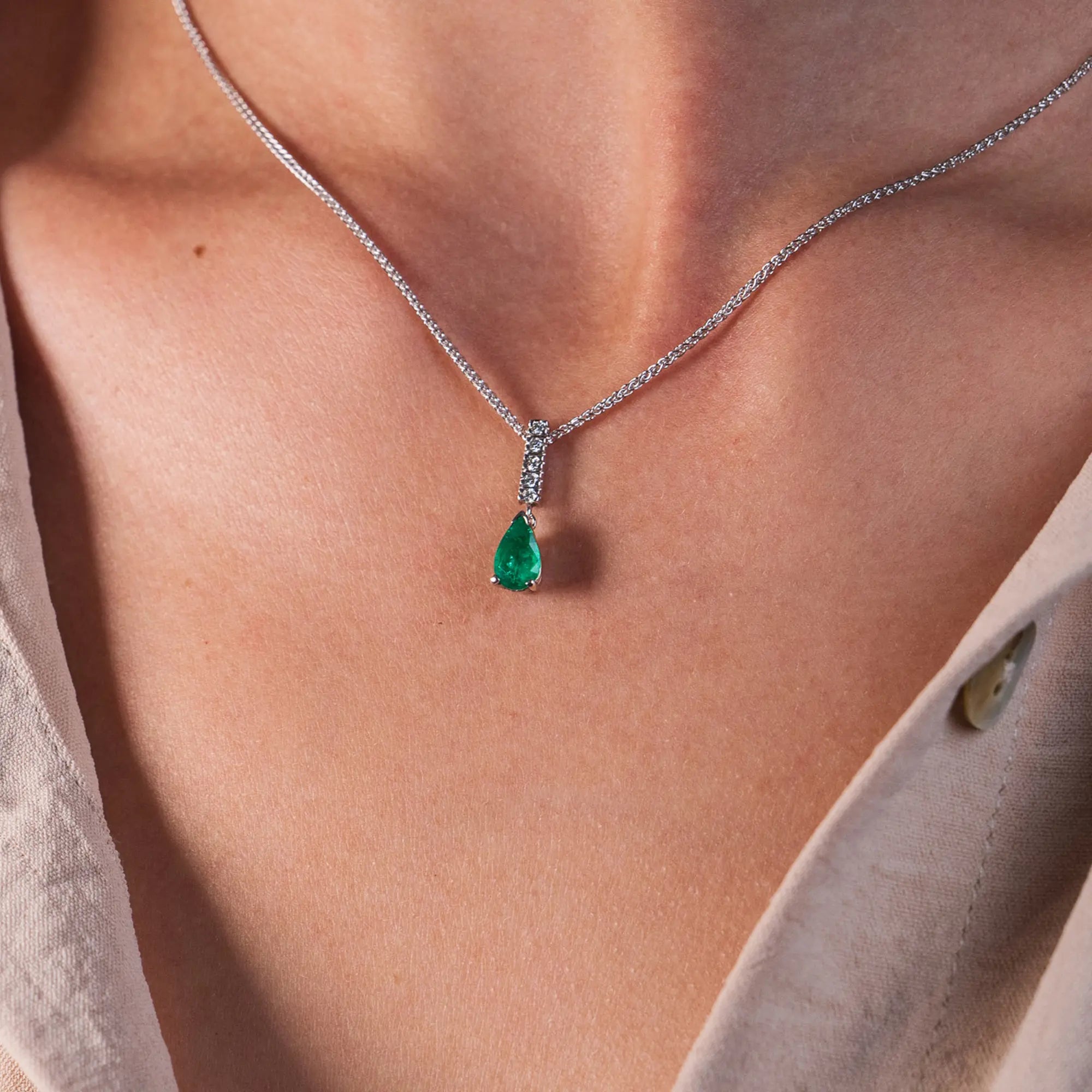 Frau trägt ein Collier aus der Schmuckatelier Lang Collection um Ihren Hals, das in Weißgold gefertigt wurde und als Highlight einen Smaragd-Anhänger in Tropfenform hängend unter einem Diamant besetzten Weißgold-Schiene