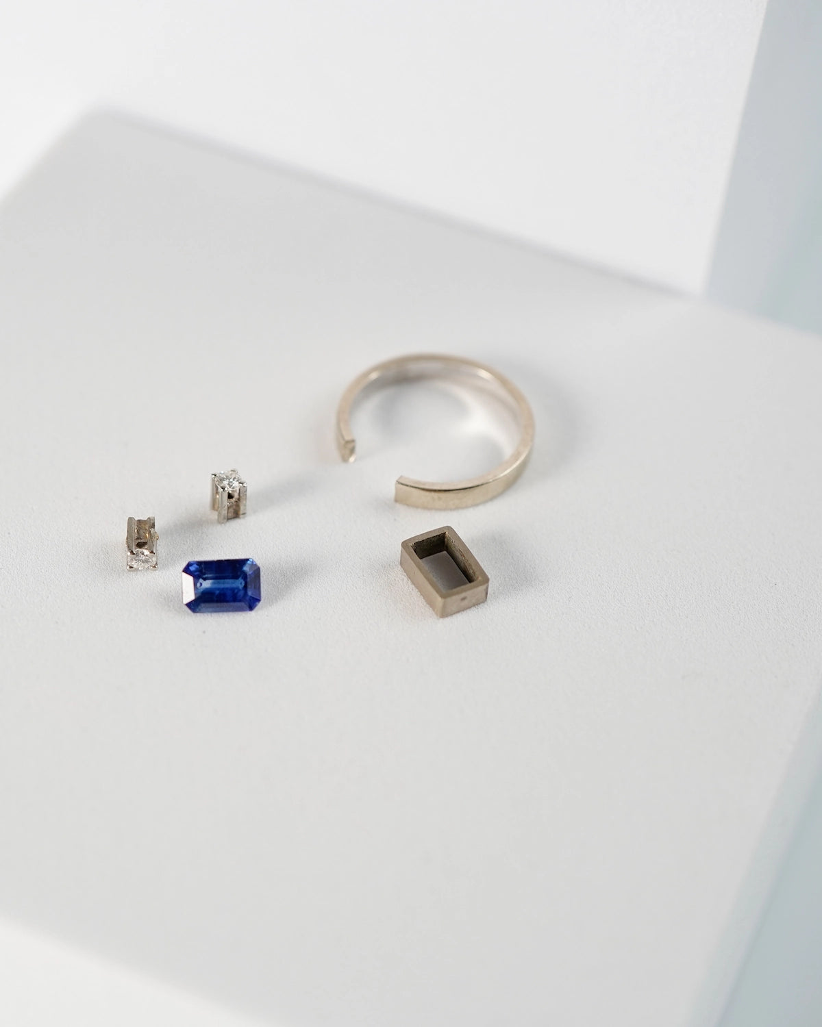 Einzelteile für einen Weißgold-Brillant-Ring, betsehend aus zwei Brillanten, einem Saphir, einer Ringeschiene und der Fassung