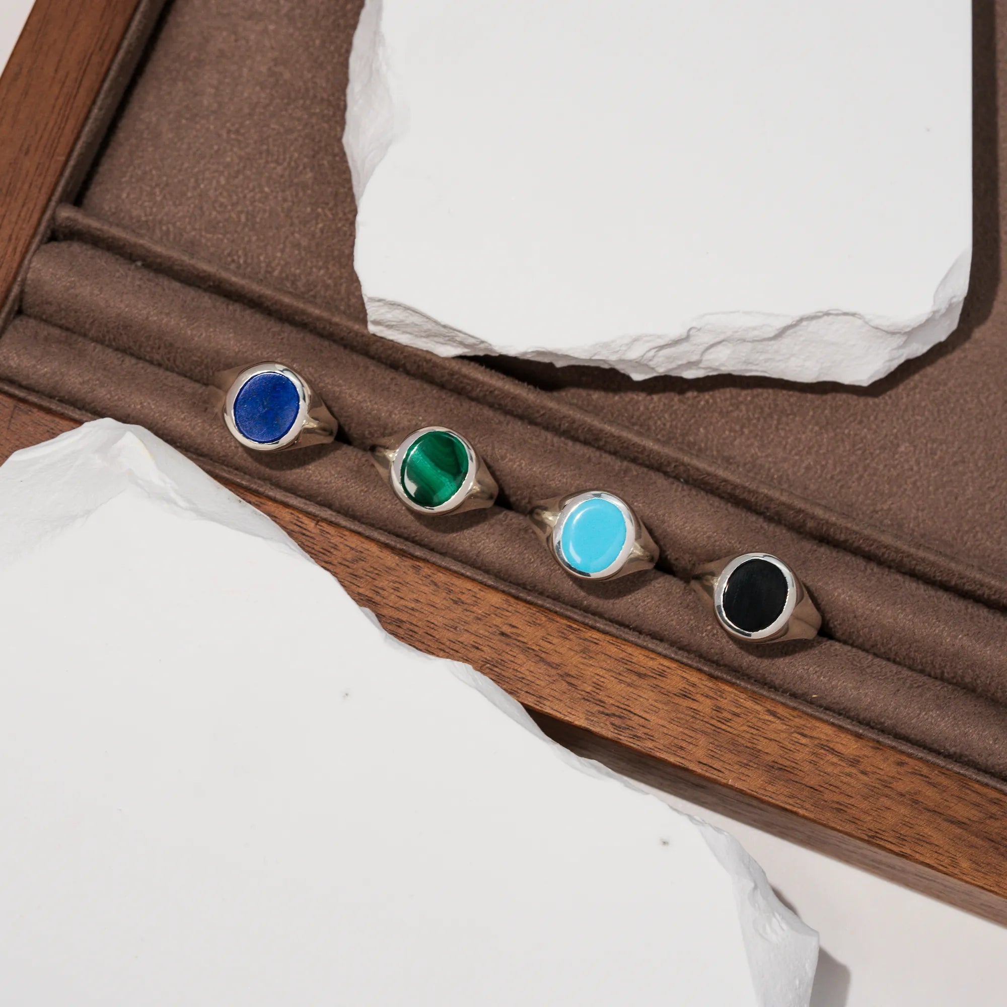Produktfotografie auf einem braunem Holztablett mit den vier aus Silber handgefertigten Siegelringe aus der Schmuckatelier Lang Collection mit Malachit, Onyx, Türkis oder Lapis Lazuli