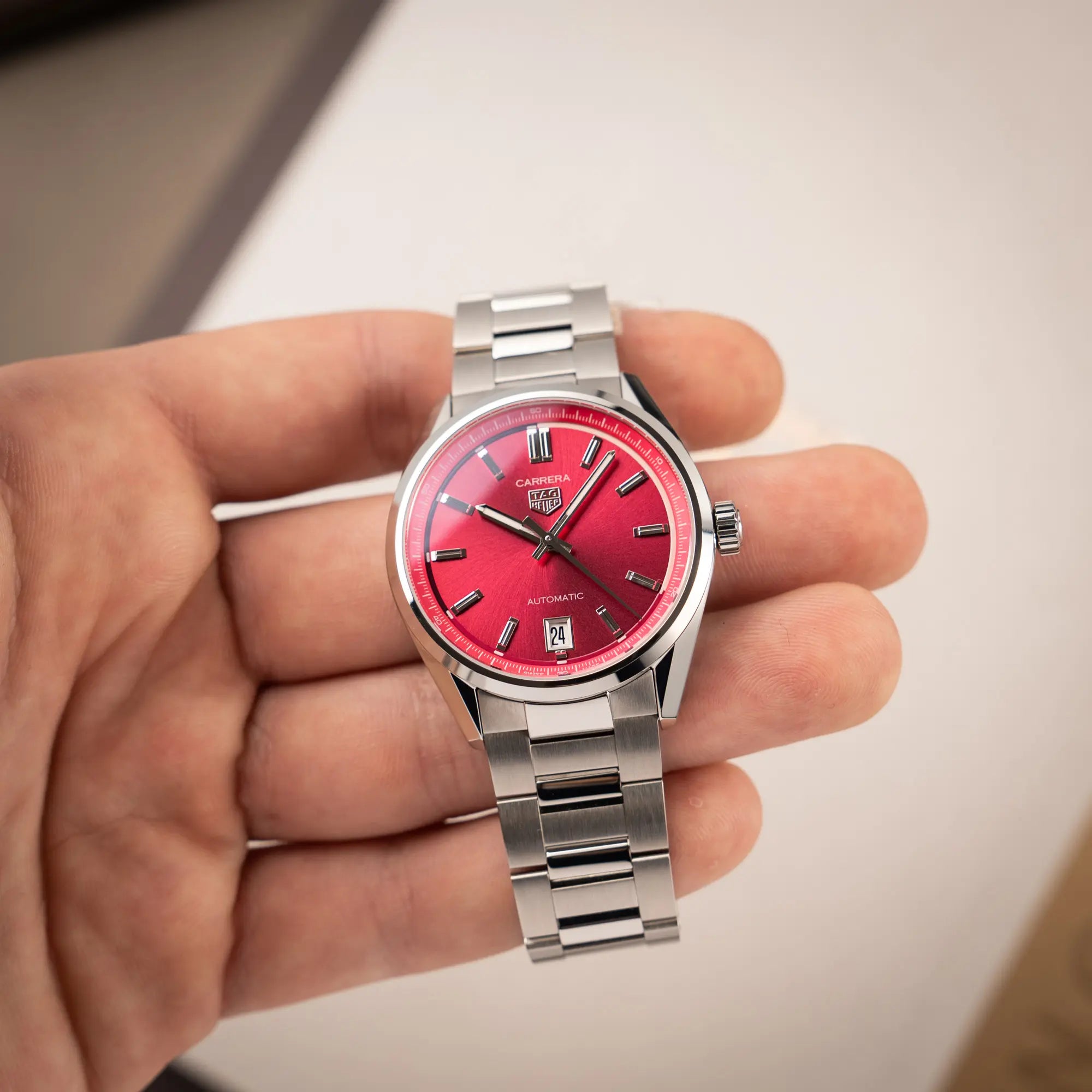 Mann hält die Damenuhr Tag Heuer Carrera Date Lady mit einem 36mm-Gehäuse und einem markanten pinken Zifferblatt mit Sonnenschliff-Finish in seiner Hand und präsentiert die Uhr in die Kamera