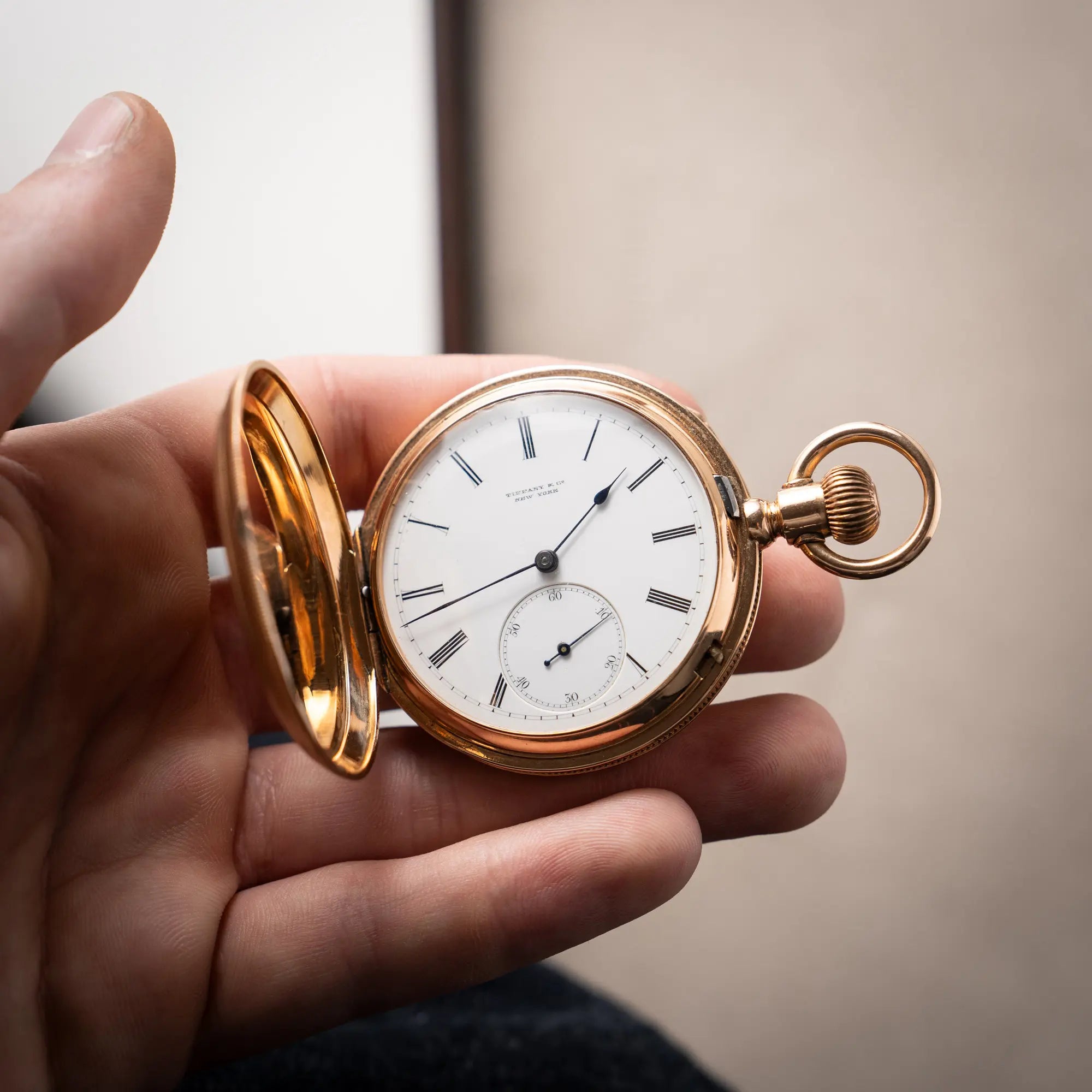 Mann hält die Tiffany & Co Savonette Taschenuhr aus 18k Gelbgold mit weißem Zifferblatt und römischen Indizes in seiner Hand