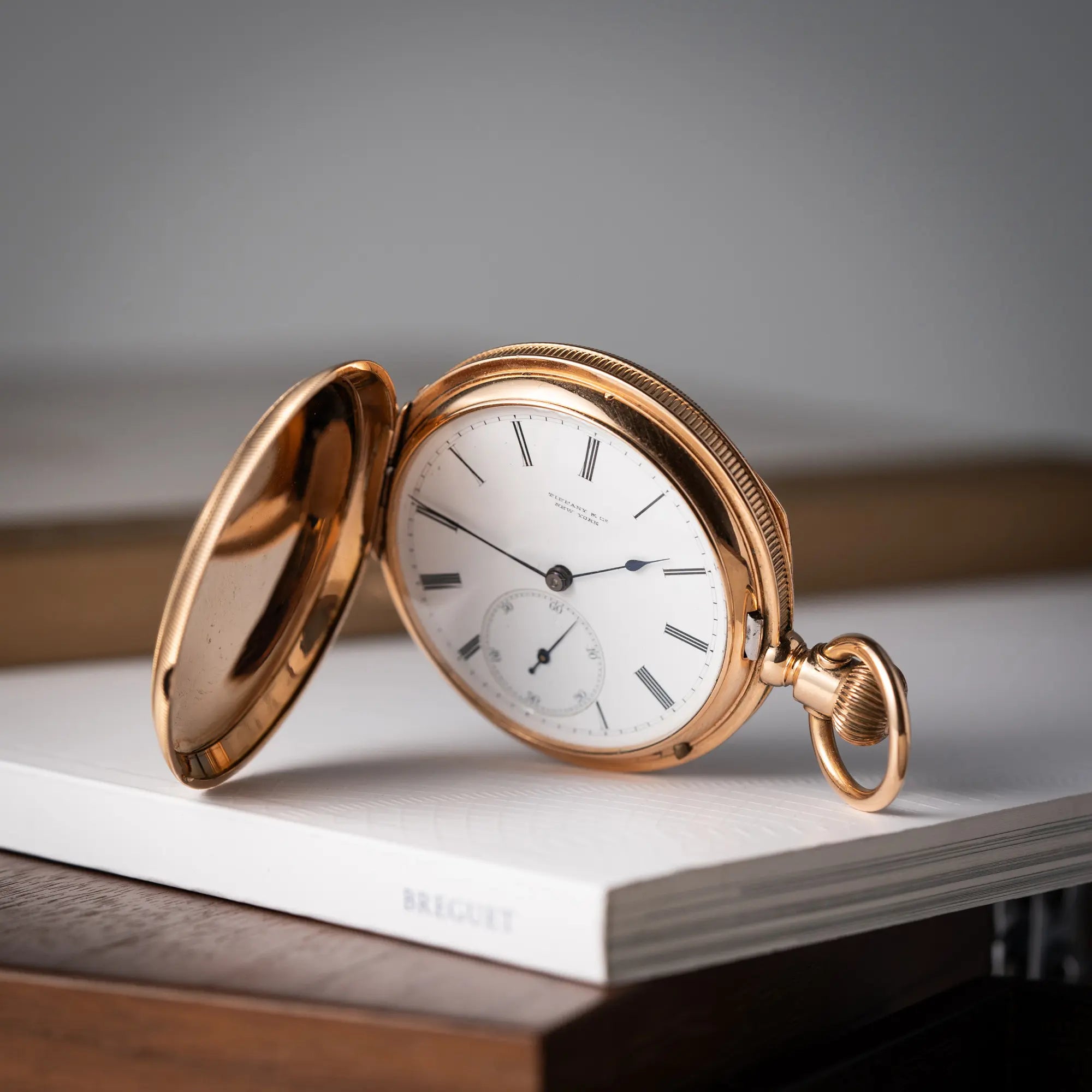 Produktfotografie der Tiffany & Co Savonette Taschenuhr aus 18k Gelbgold mit weißem Zifferblatt und römischen Indizes mit aufgeklapptem Gehäusedeckel