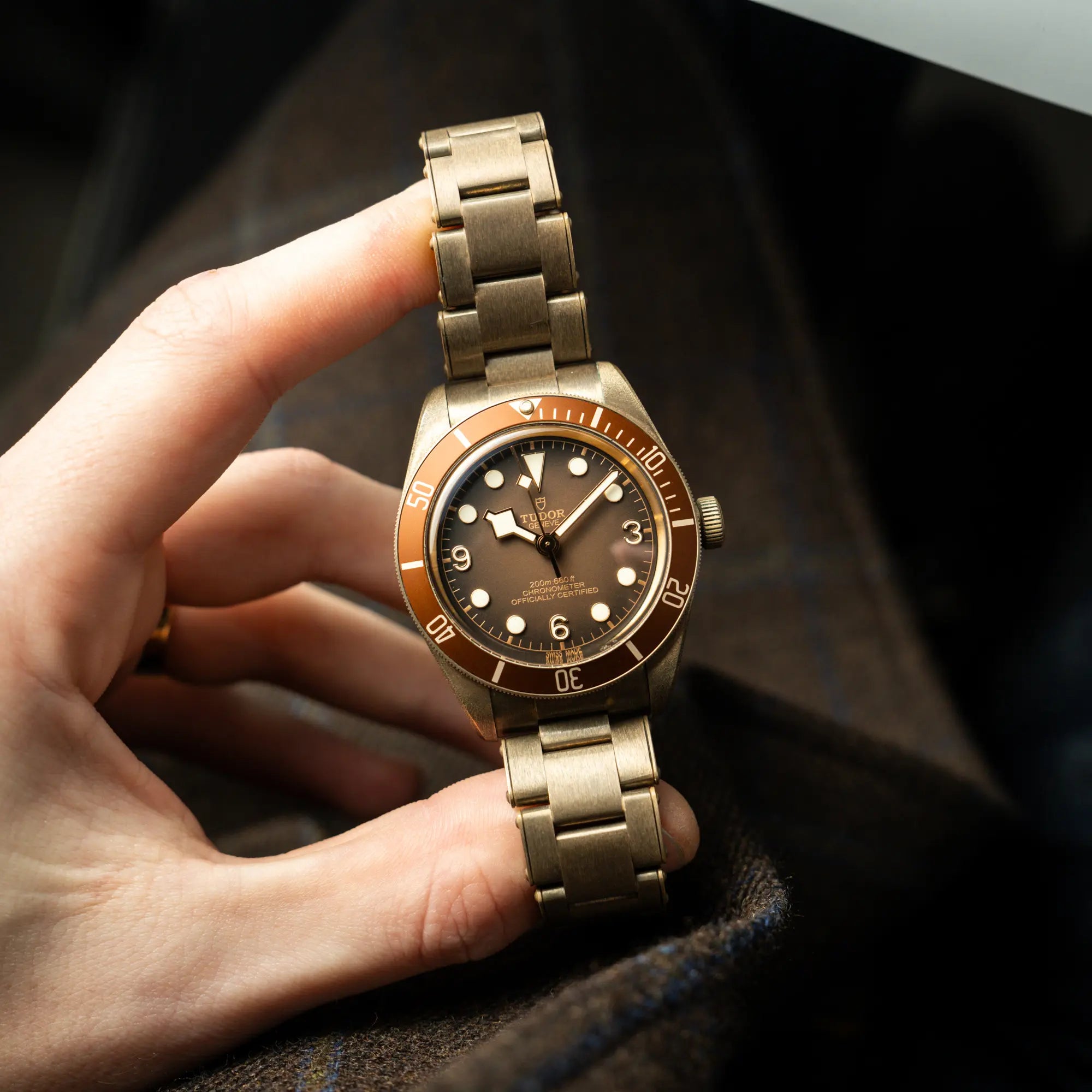 Mann hält die Tudor Black Bay 58 M79012M in Bronze, deren Oberfläche bereits mit einer gleichmäßigen Patina überzogen ist, mit einem braunem Zifferblatt zwischen Daumen und Zeigefinger