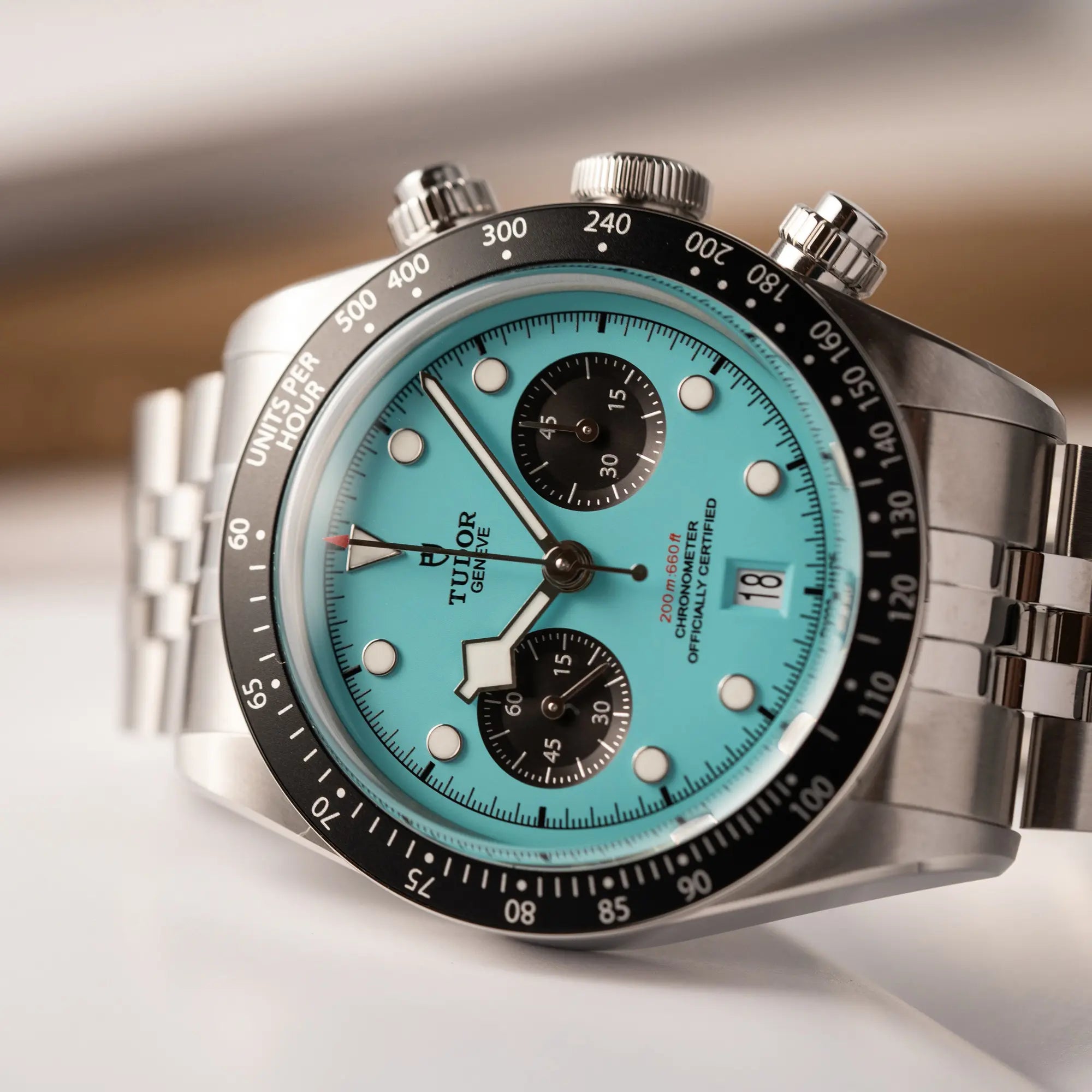 Detailaufnahme von dem seitlich auf dem Uhrengehäuse liegenden Tudor Black Bay Chronograph Flamingo mit dem türkis-blauen Zifferblatt mit schwarzen Totalisatoren und schwarzer Lünette mit Zähler-Skala