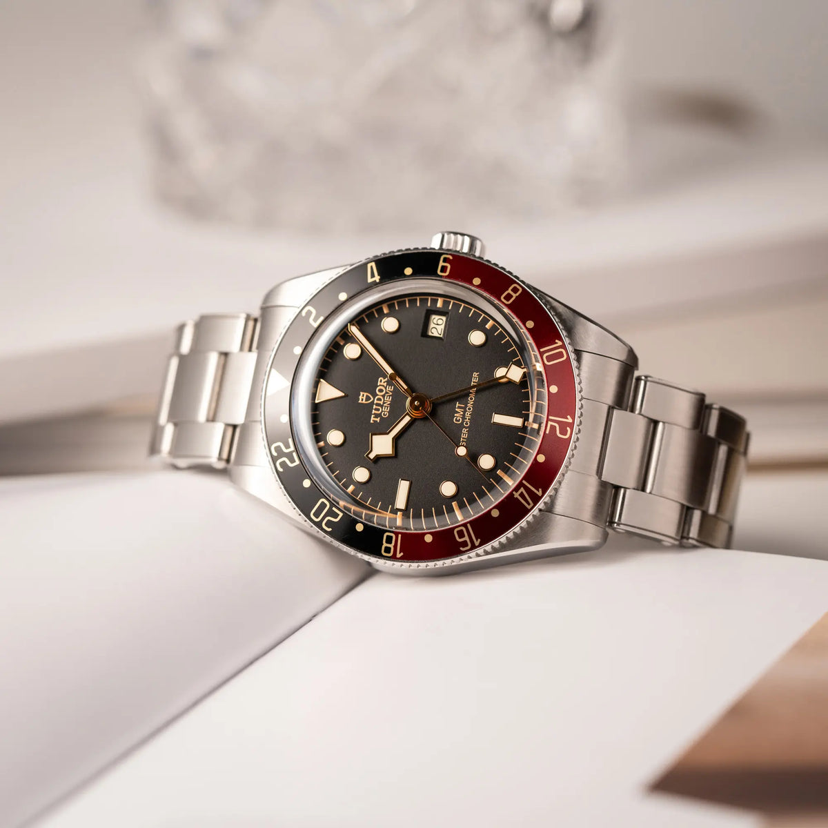 Tudor BlackBay GMT Coke der Referenz 7939G1A0NRU mit der schwarz-roten Lünette und bronzefarbenen Details am Edelstahlarmband  liegt schräg auf einem Uhrenbuch