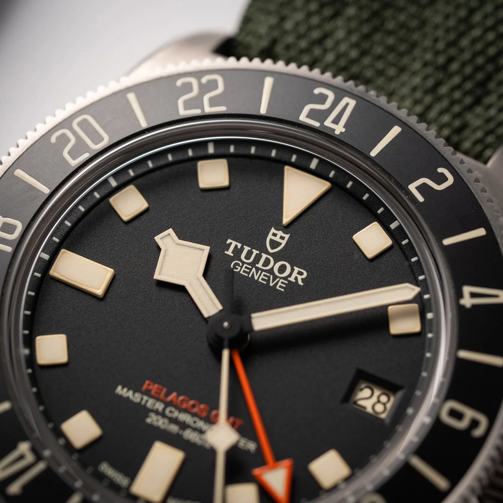 Detailaufnahme der Tudor Pelagos GMT Military der Referenz M2542G257NU-0002 mit Titan-Gehäuse und schwarzem Zifferblatt an einem olivgrünen Nato-Strap fokussiert das Tudor-Logo bei 12 Uhr