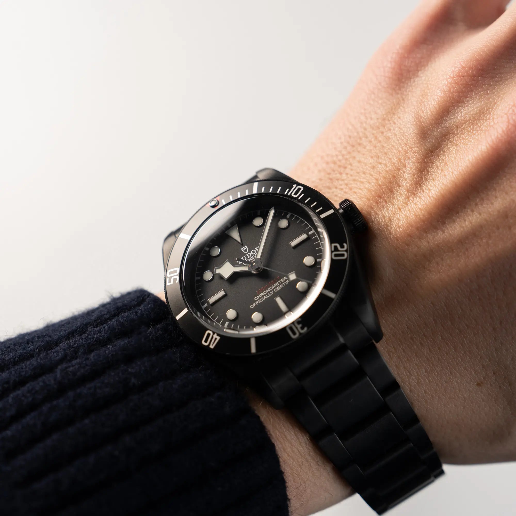 Wristshot mit Produktfotografie der seitlich liegenden Tudor Black Bay Dark 79230DK mit einem schwarz beschichteten Gehäuse und weißen Ziffern & Indizes an einem männerhandgelenk