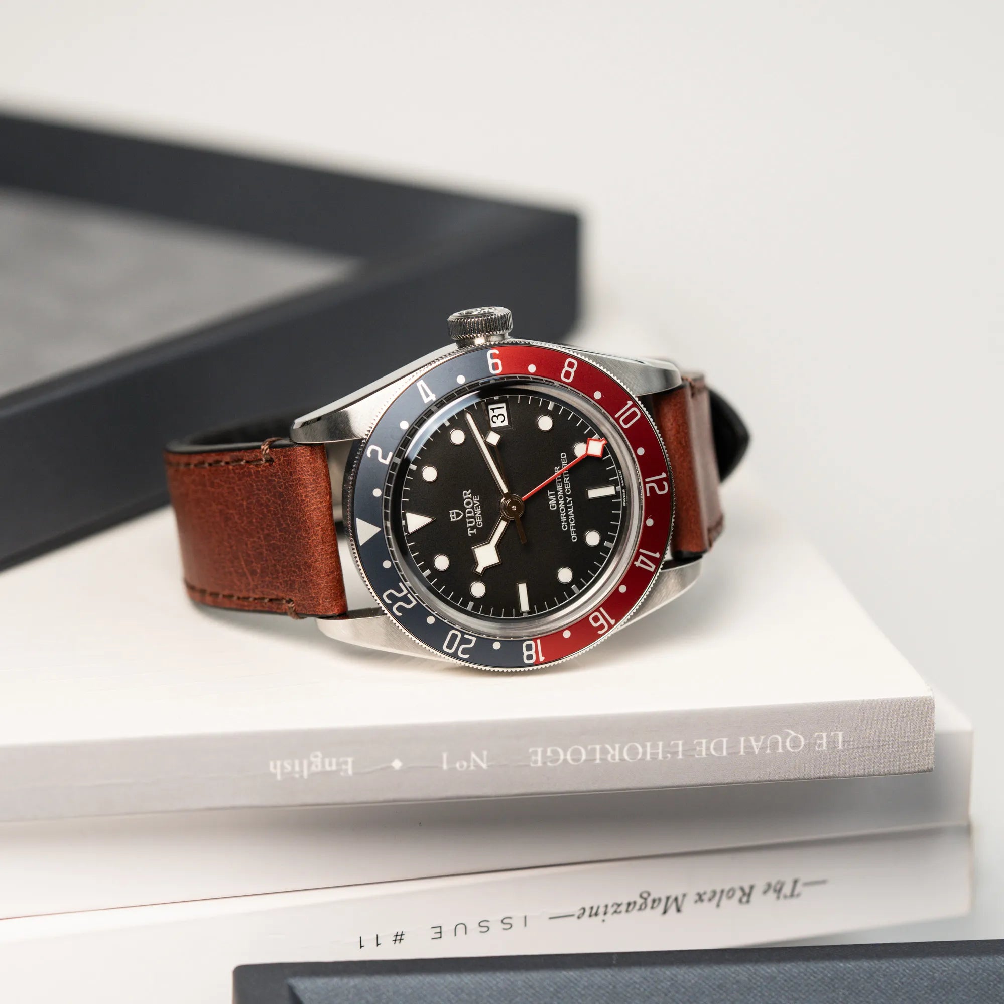 Produktfotografie der Tudor Black Bay Pepsi mit der Referenz 97830RB am braunen Lederband im Neuzustand, während die Uhr auf einem Horologie Buch liegt